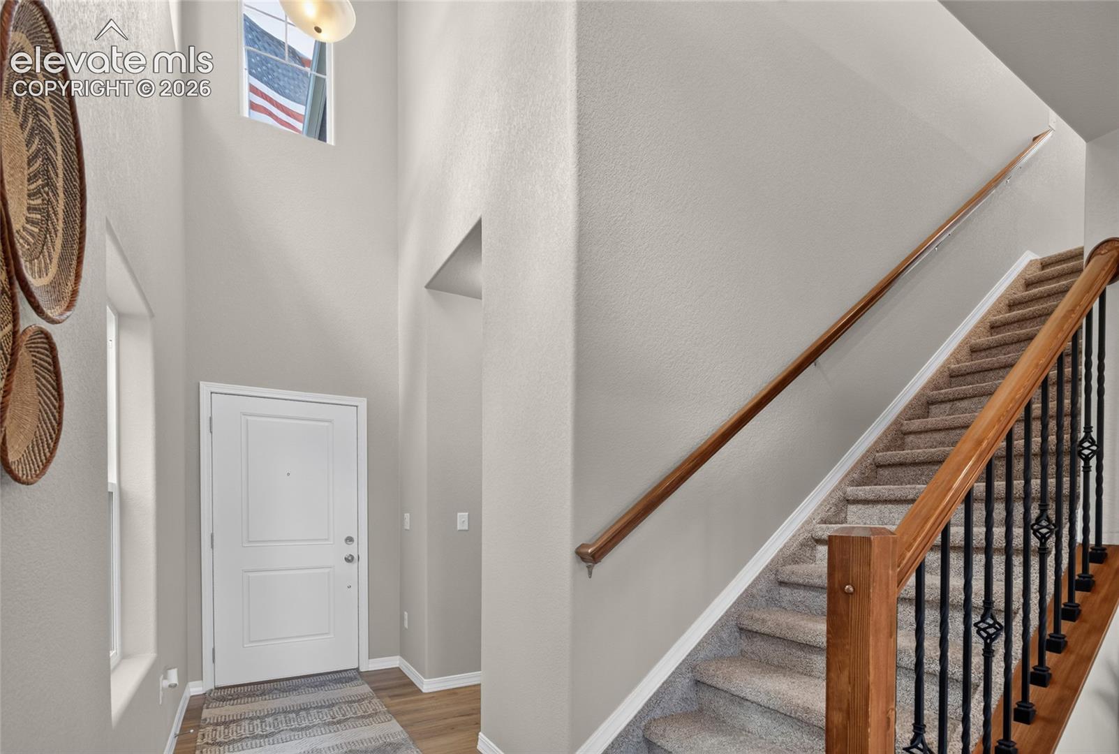 Foyer featuring high ceilings, natural light, a wood-finish handrail, decorative iron balusters, and carpeted stairs
