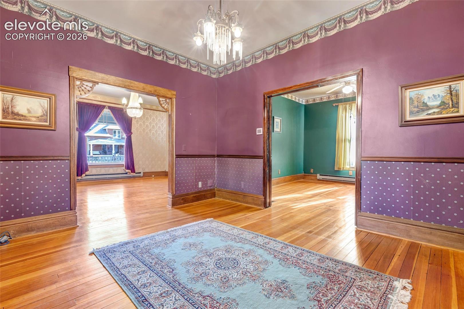 Interior space featuring wood-finish flooring, intricate crown molding, detailed wall trim, wide wood-encased doorways, and an ornamental glass chandelier