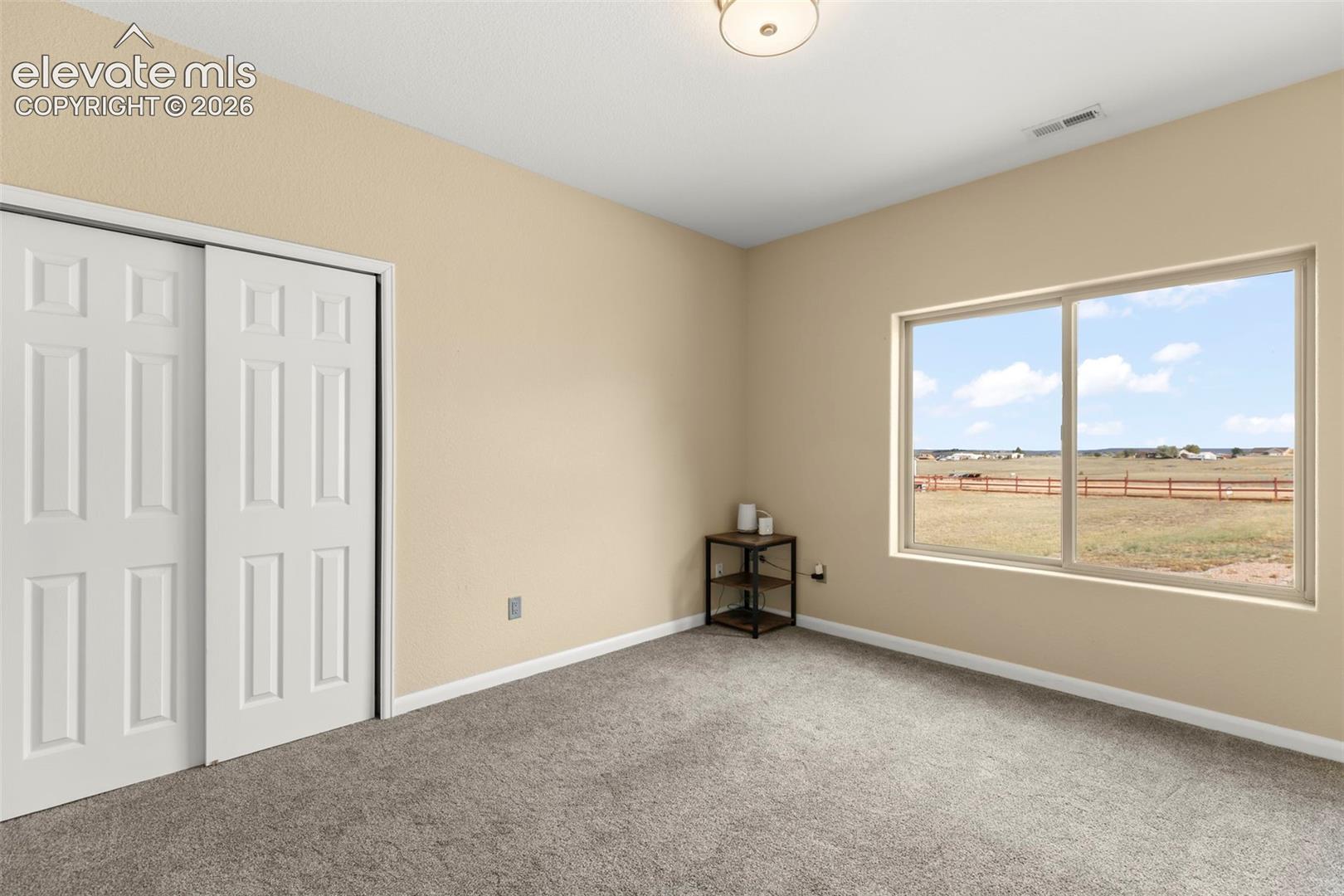 Room featuring neutral wall tones, carpet flooring, a multi-panel sliding closet door, and a large horizontal window with exterior rural scenery