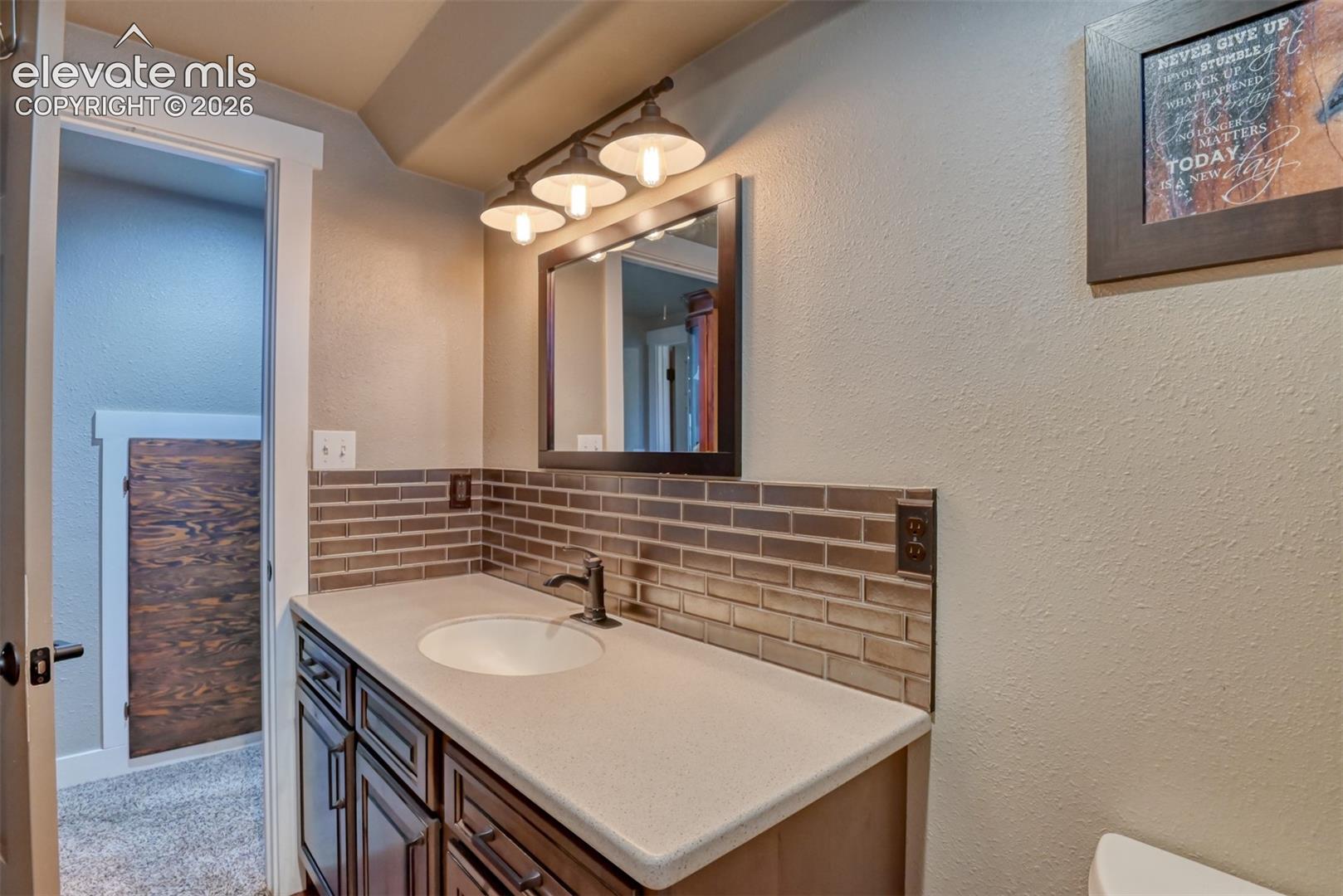 Bathroom featuring decorative backsplash, a textured wall, and vanity