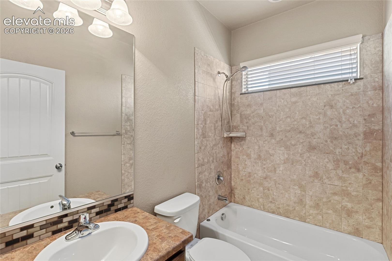 Bathroom featuring a vanity with a drop-in sink, a large wall-mounted mirror, a tiled shower-tub combination, and a horizontal window