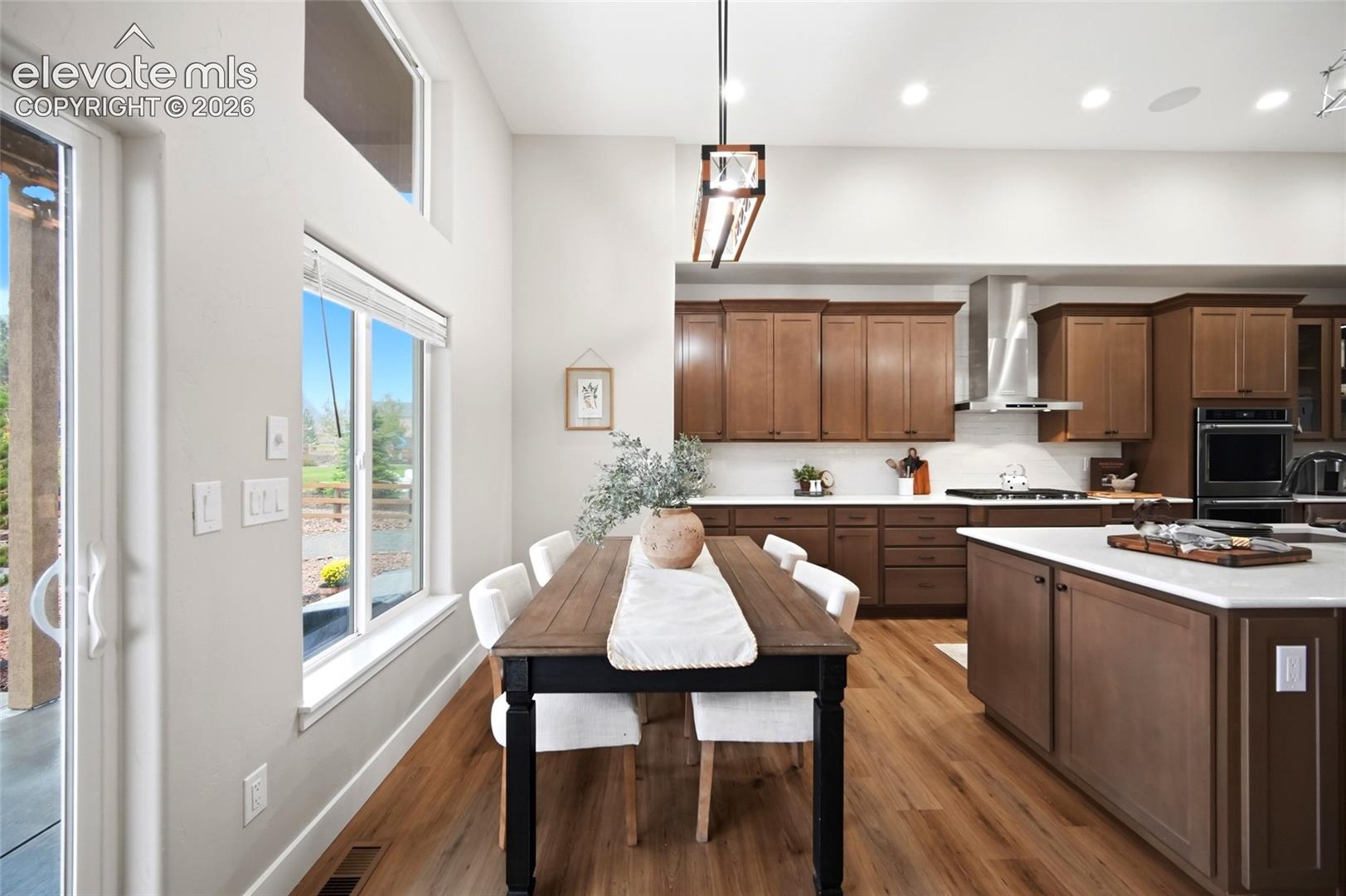 Kitchen featuring wood-finish flooring, wood cabinetry, a center island with a solid-surface countertop, stainless steel range hood, and tall windows