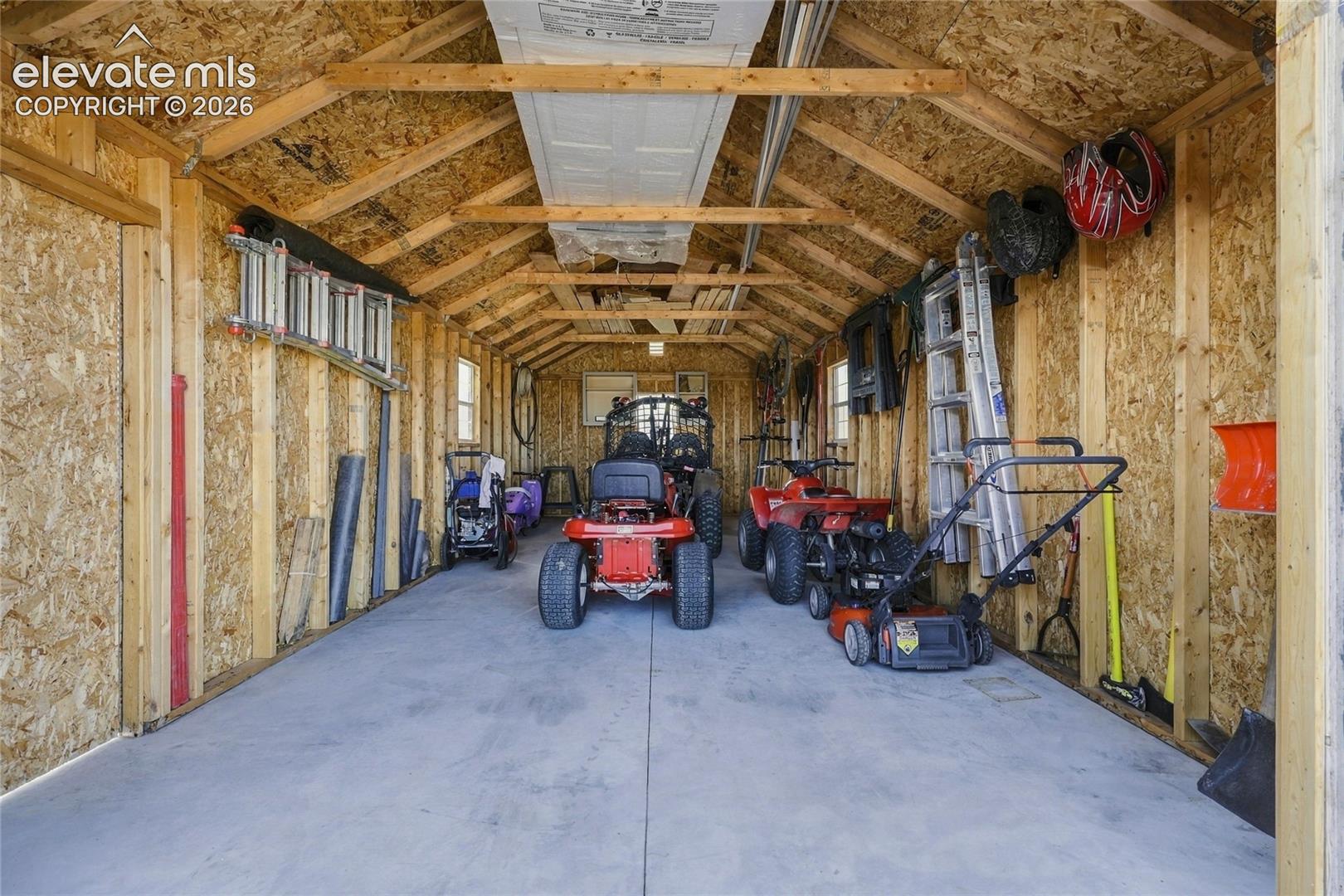 Detached storage building featuring exposed wood-frame construction, concrete flooring, dual windows, and vaulted ceiling design