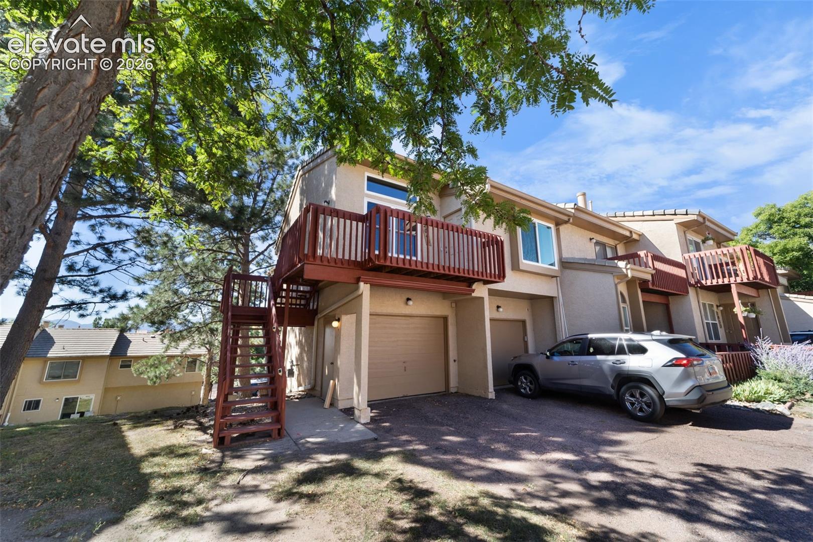 Stucco exterior with wood-slat balcony railing, integrated garage, and external wooden staircase