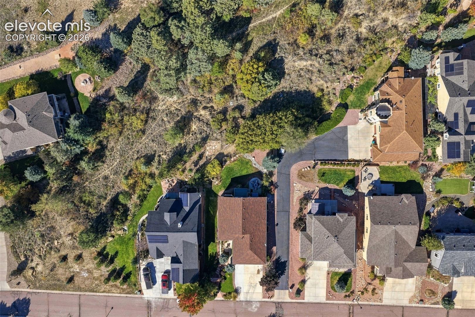 Aerial perspective of residential properties featuring asphalt driveways, mature coniferous and deciduous landscaping, and multi-pitched rooflines with integrated solar panel arrays
