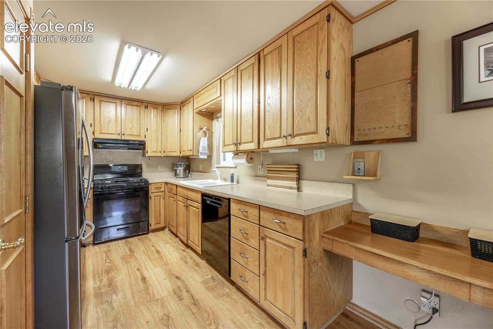 Kitchen featuring natural wood cabinetry, solid surface countertops, wood-finish flooring, and black appliances