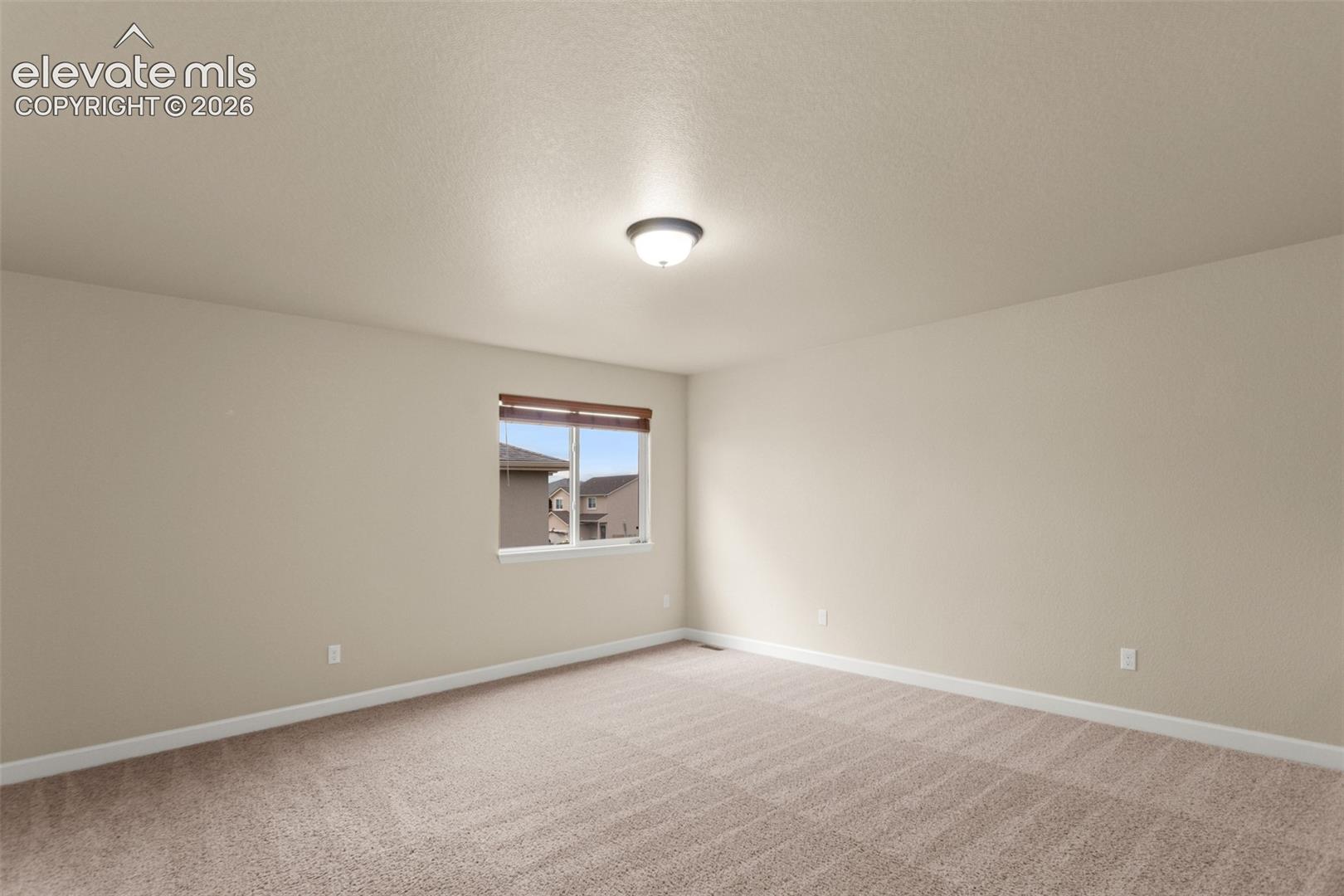 Neutral-toned interior space featuring wall-to-wall carpeting, a single-pane window with wood-finish blinds, and a central ceiling-mounted light fixture
