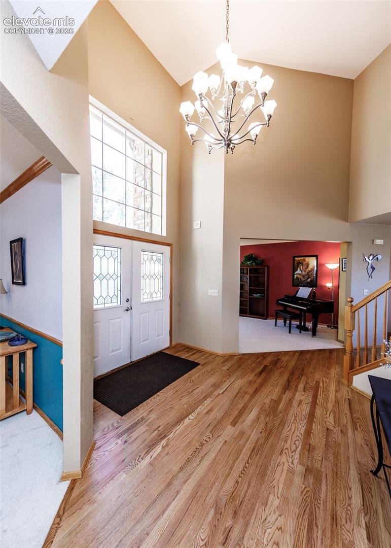 Foyer featuring wood-finish flooring, a vaulted ceiling, a decorative chandelier, and a transom window above double entry doors
