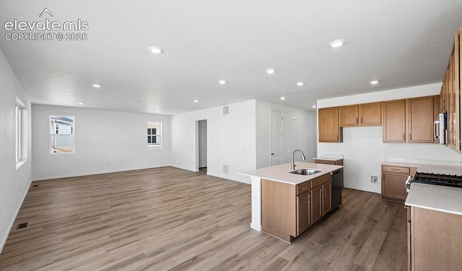 Kitchen featuring wood-finish cabinetry, stone-style countertops, an island with an undermount sink, recessed lighting, and wood-finish flooring