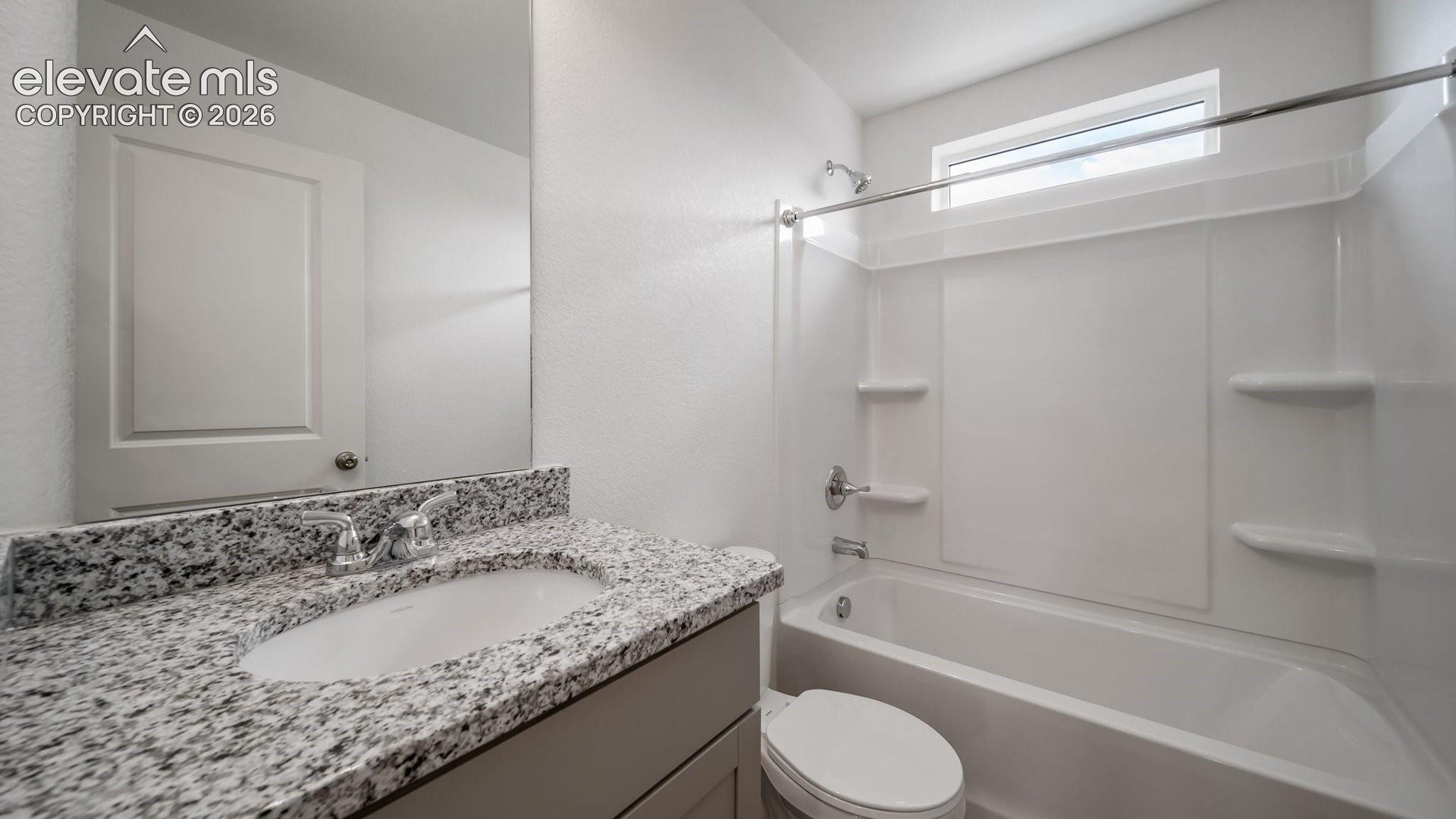 Vanity with stone countertop and undermount sink, chrome faucet, full-width mirror, and a shower-tub combination with overhead window
*photos of a model home*