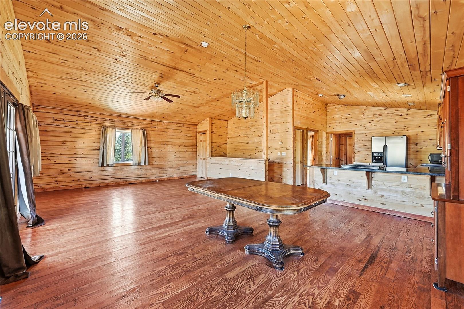 Expansive room featuring wood-paneled walls and ceiling, wood-finish flooring, and a breakfast bar with stainless steel appliances
