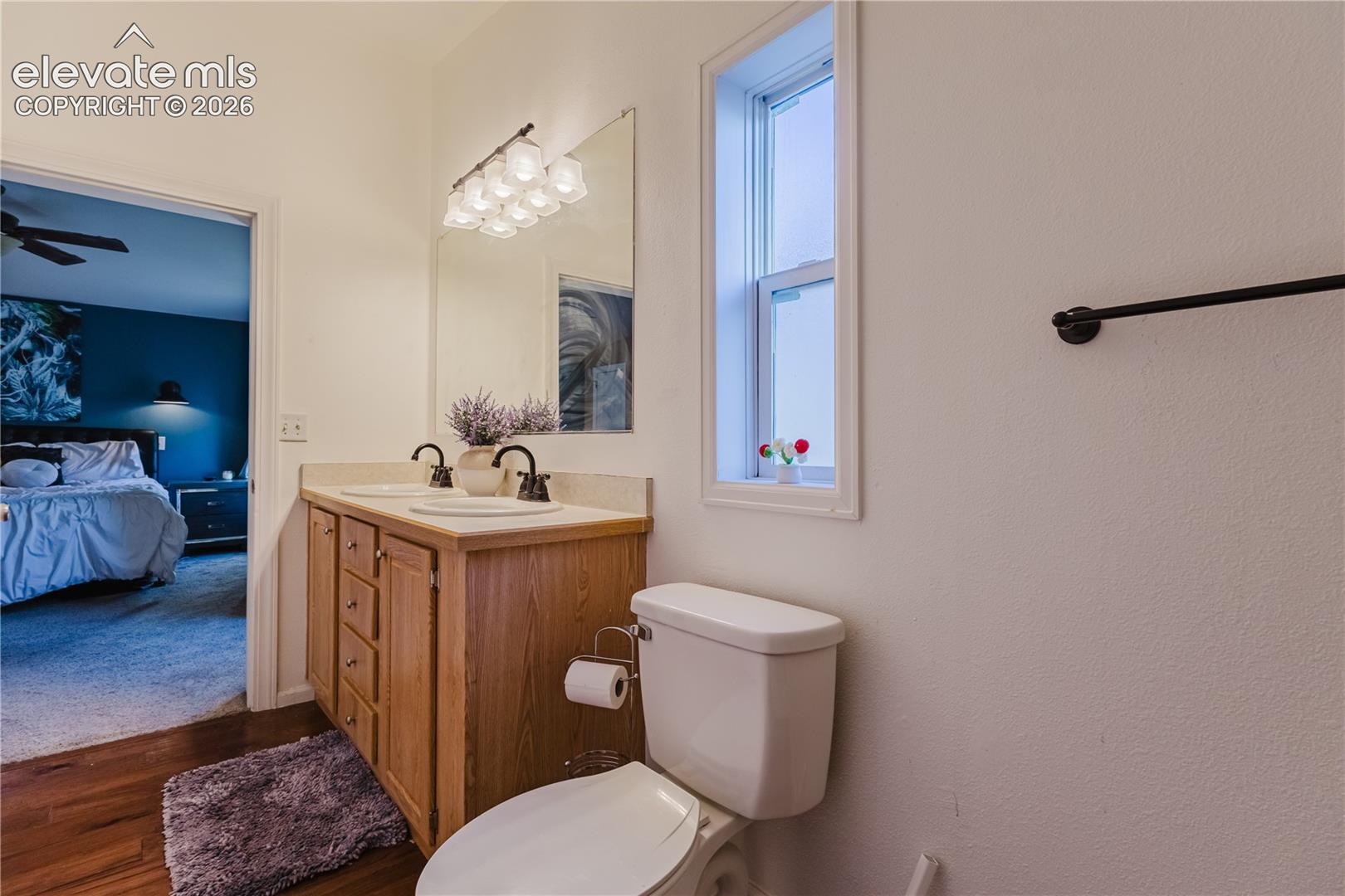 Wood-finish flooring, dual basin vanity with wood cabinetry, and a single window