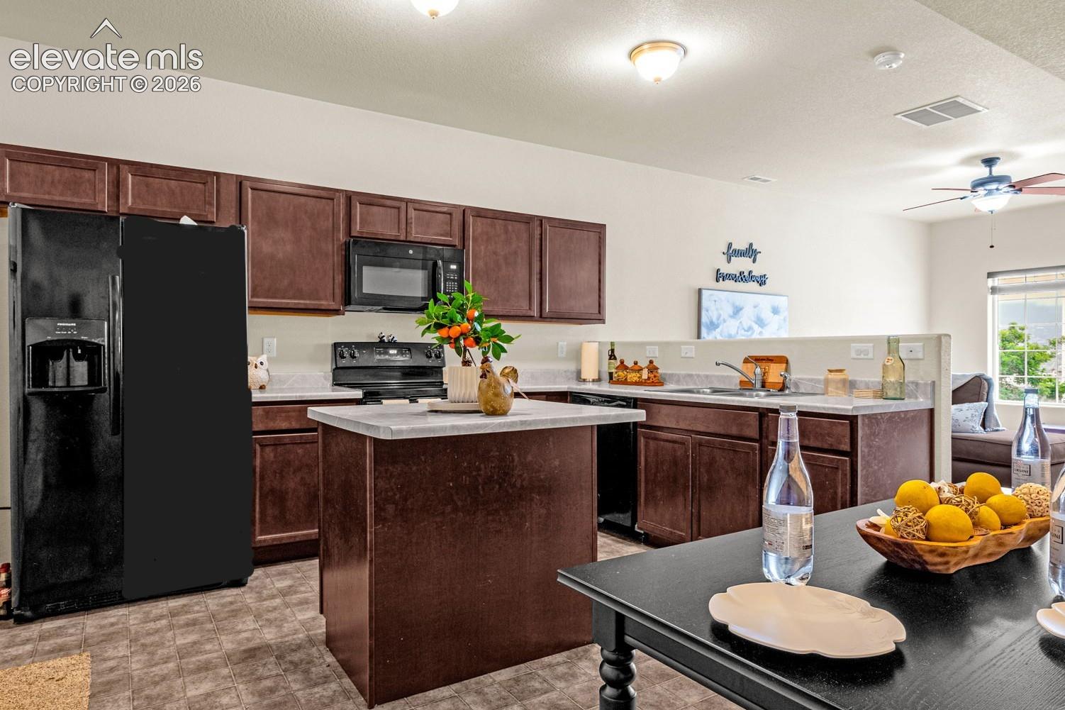 Kitchen featuring dark wood-finish cabinetry, black appliances, a central island, and light countertops