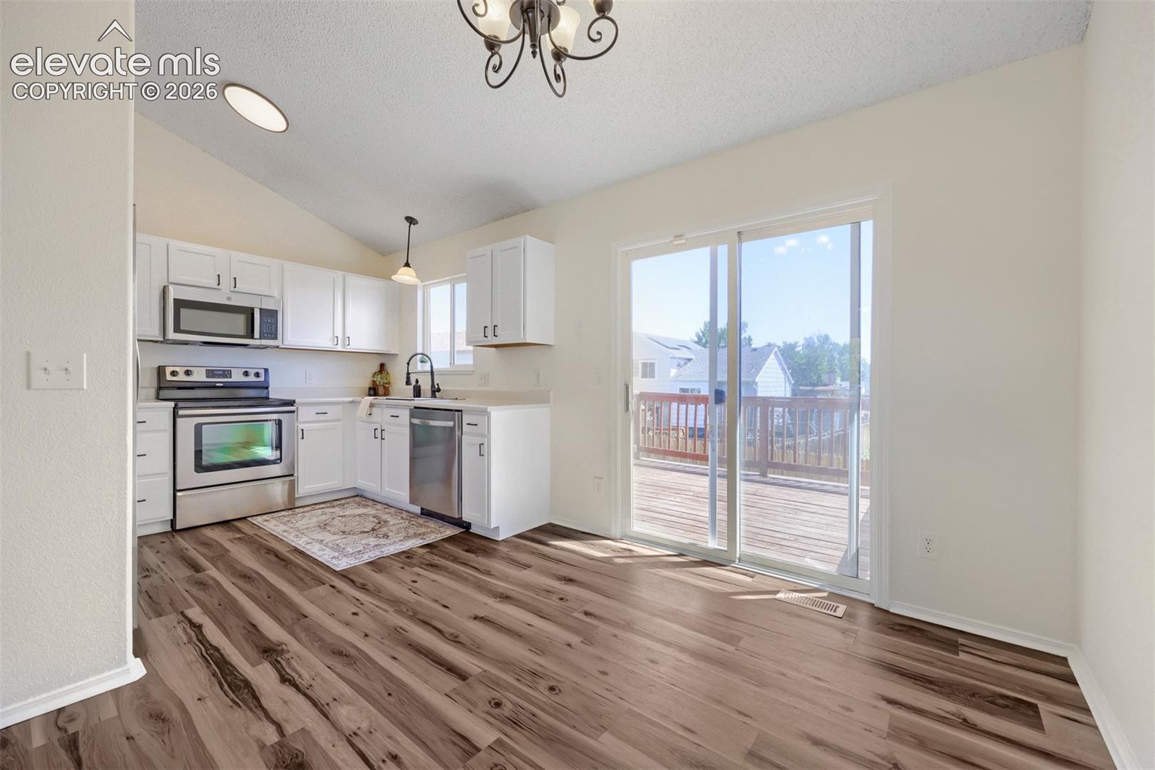 Kitchen featuring white cabinetry, stainless steel appliances, wood-finish flooring, a vaulted ceiling, and direct access to an outdoor deck