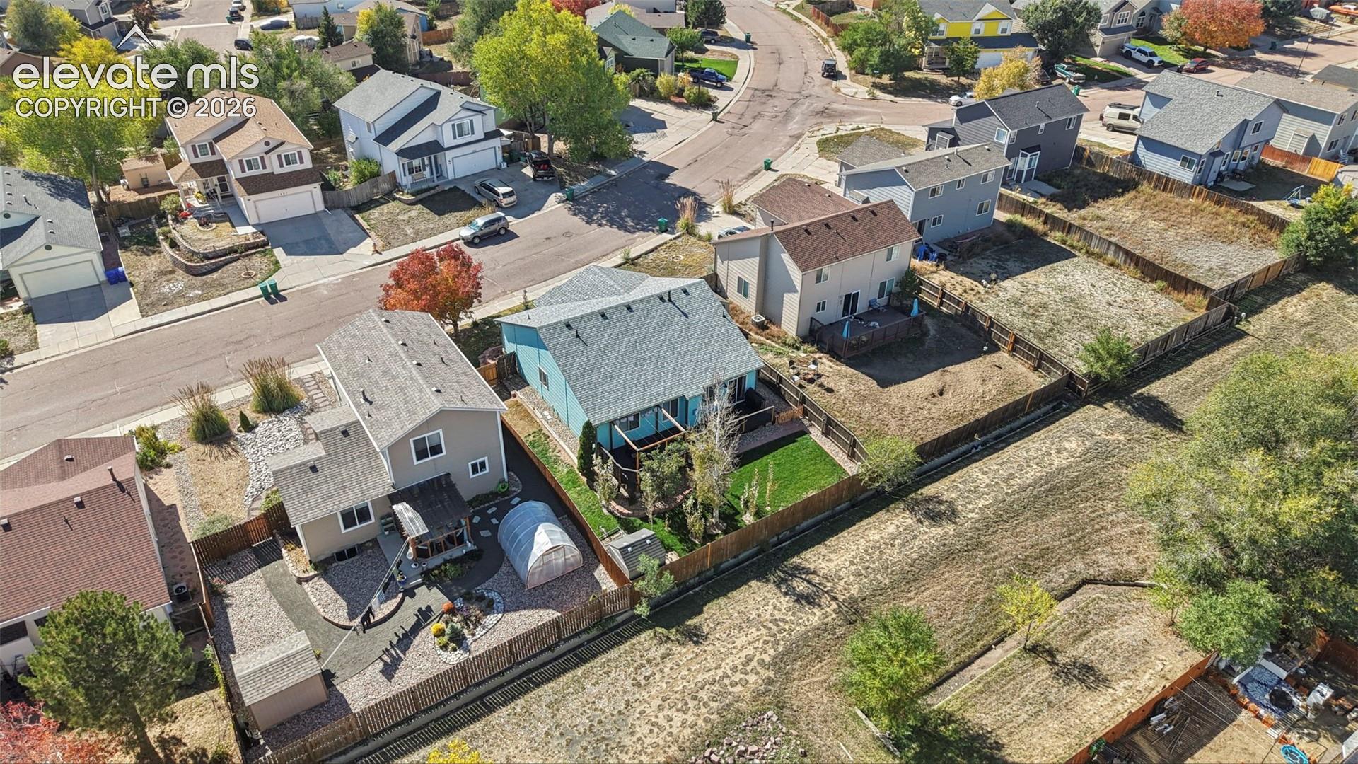 Aerial perspective featuring residential lots with fenced perimeters, paved street access, varied landscaping, and rear-yard hardscaping