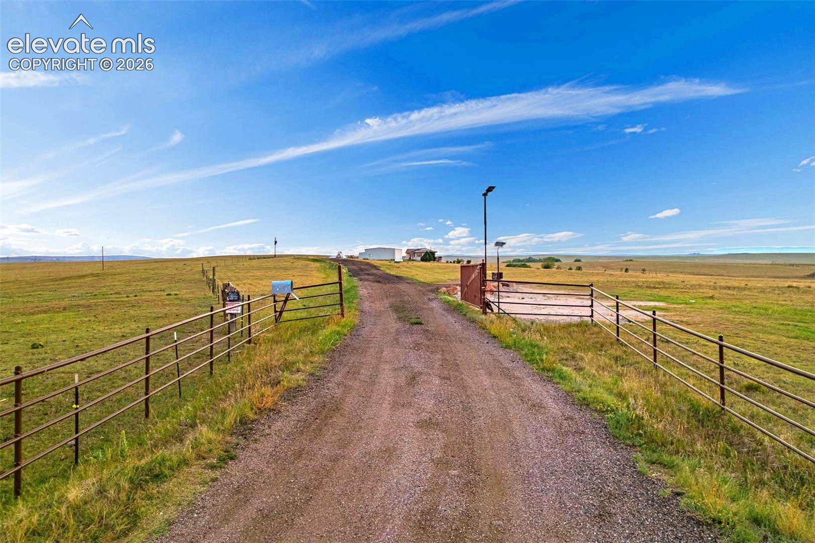 Expansive open land with a gravel driveway, metal fencing, and a main gate