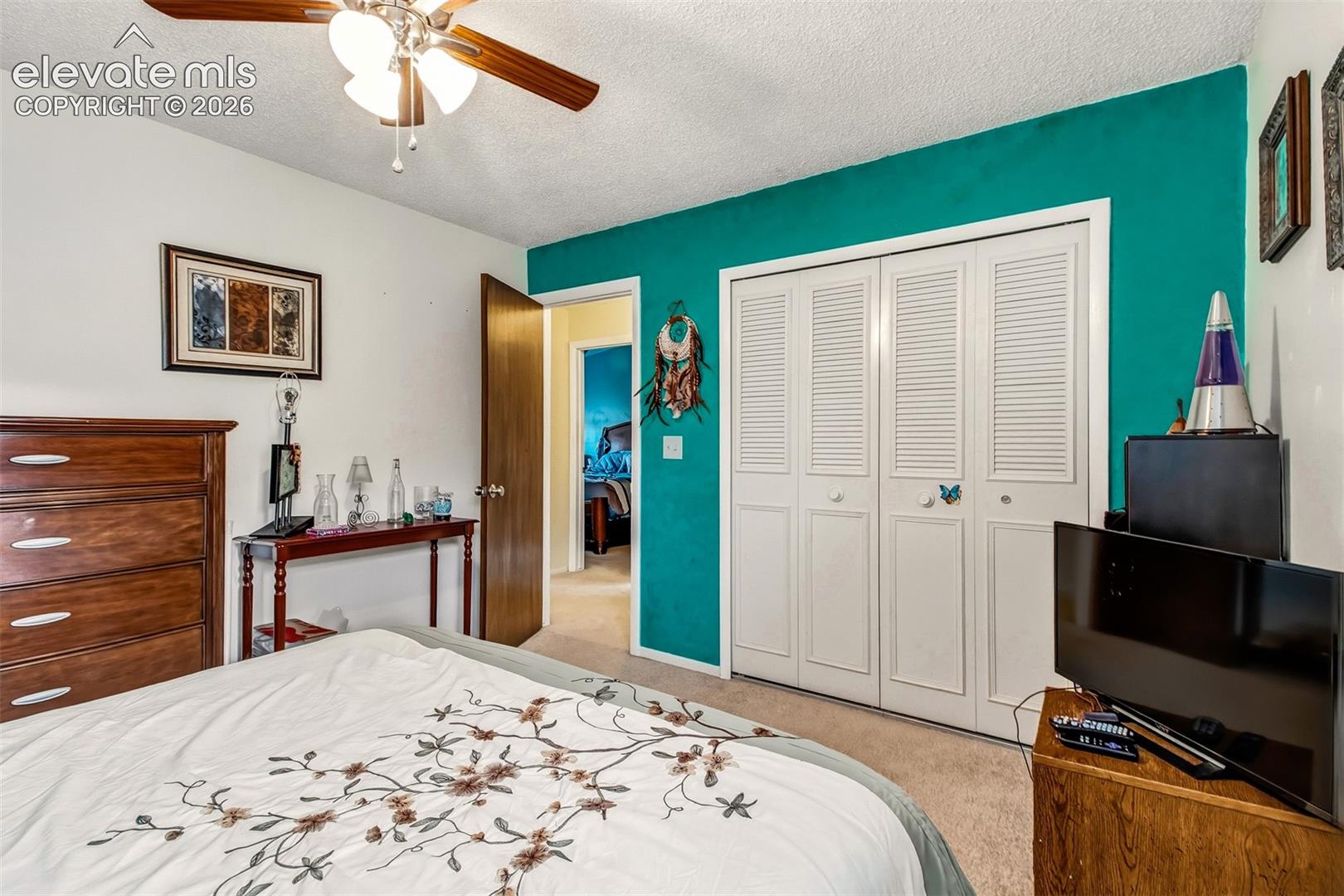 Bedroom featuring carpeted flooring, a ceiling fan with light fixture, and a white, four-panel louvered closet door