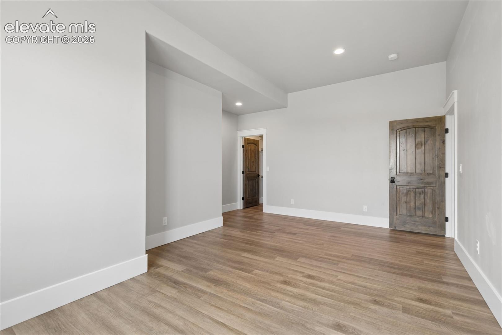 Spacious room featuring wood-finish flooring, light gray walls, white trim, and recessed lighting