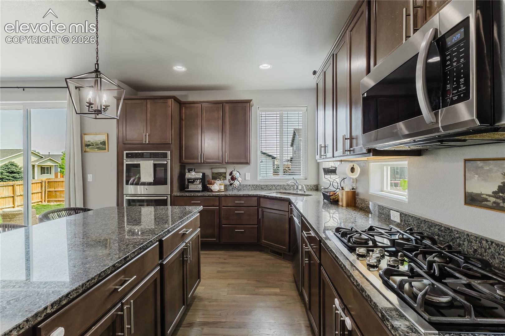 Kitchen featuring dark wood cabinetry, granite countertops, wood-finish flooring, a stainless steel gas range, and a built-in double oven