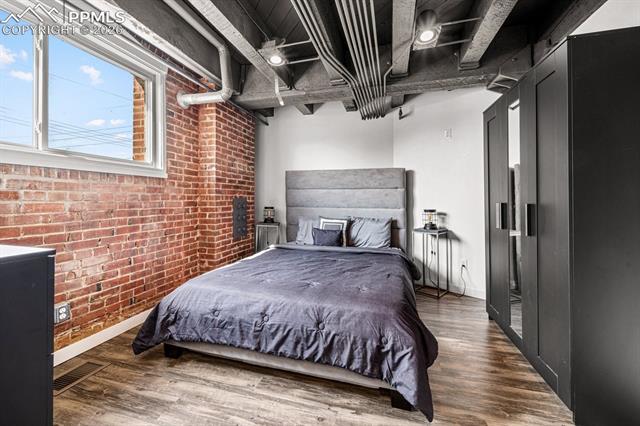 Bedroom featuring brick wall and wood finished floors