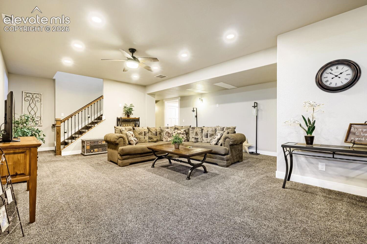Recessed lighting, ceiling fan, carpeted flooring, wood-finish stair railing with wrought iron balusters, and white wall paint