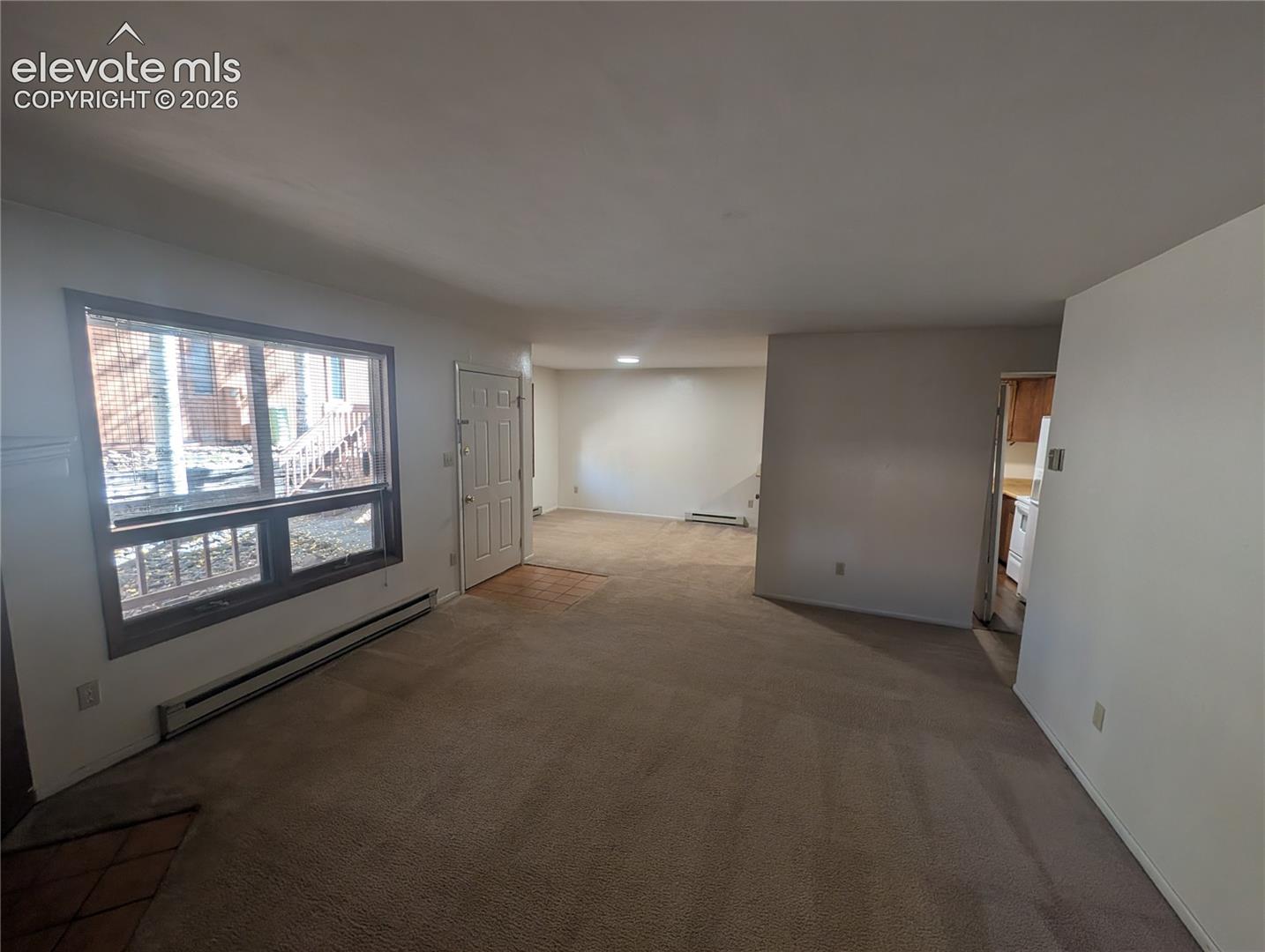 Carpeted living space with a front entry door, a large window, and baseboard heating