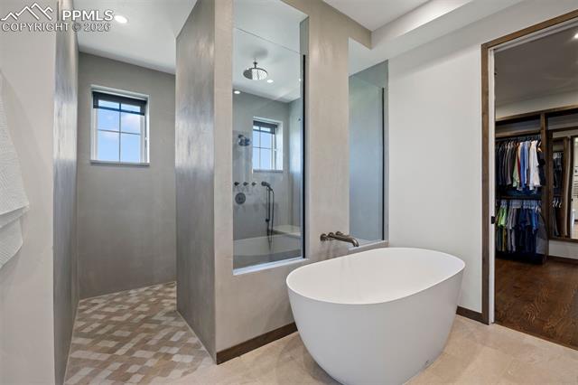 Primary bath with freestanding soaking tub, oversized walk-in shower with rain head, and custom walk-in closet beyond.