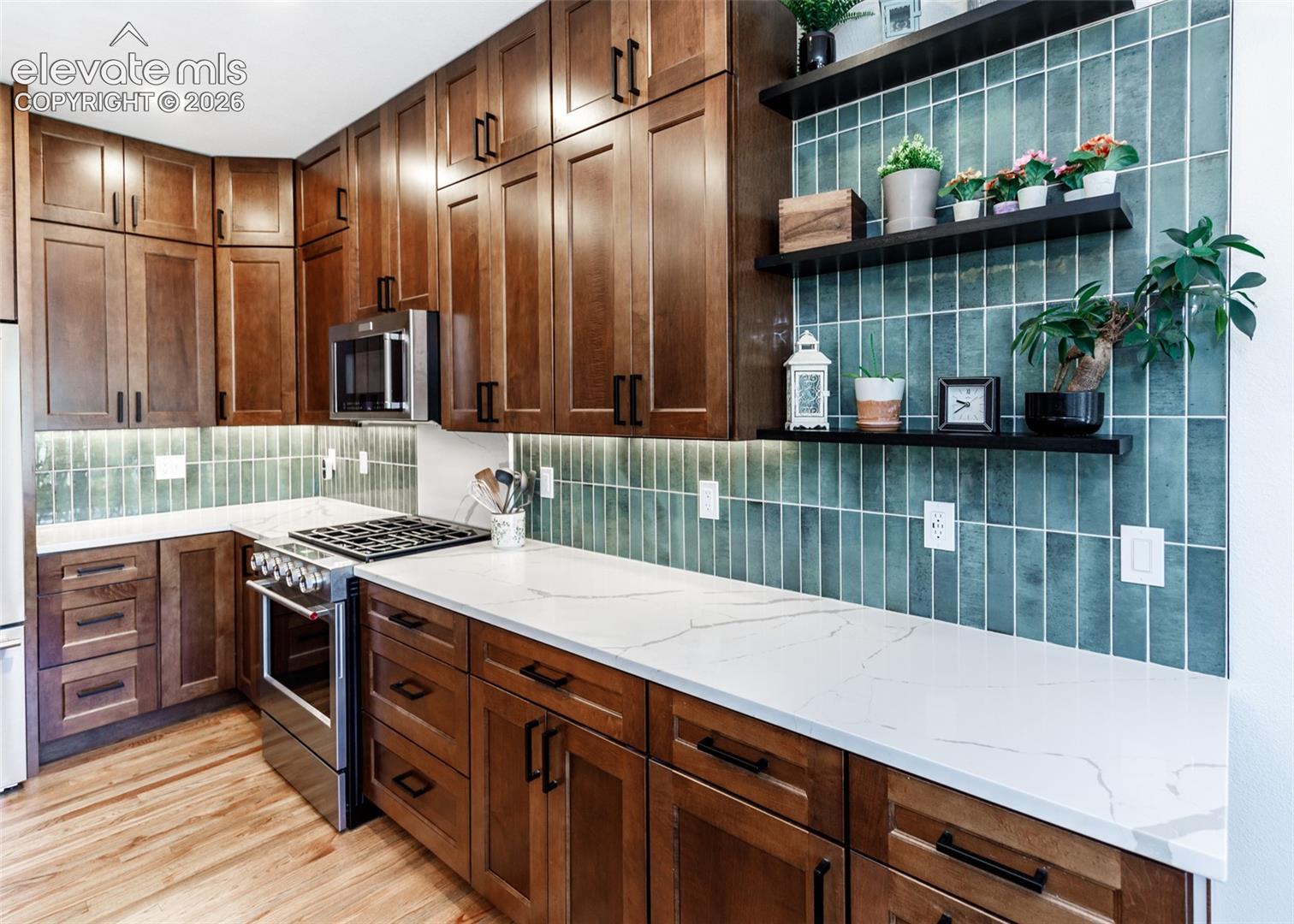 Hardwood flooring, custom wood cabinetry, stainless steel appliances, white countertops, and a full-height tile backsplash