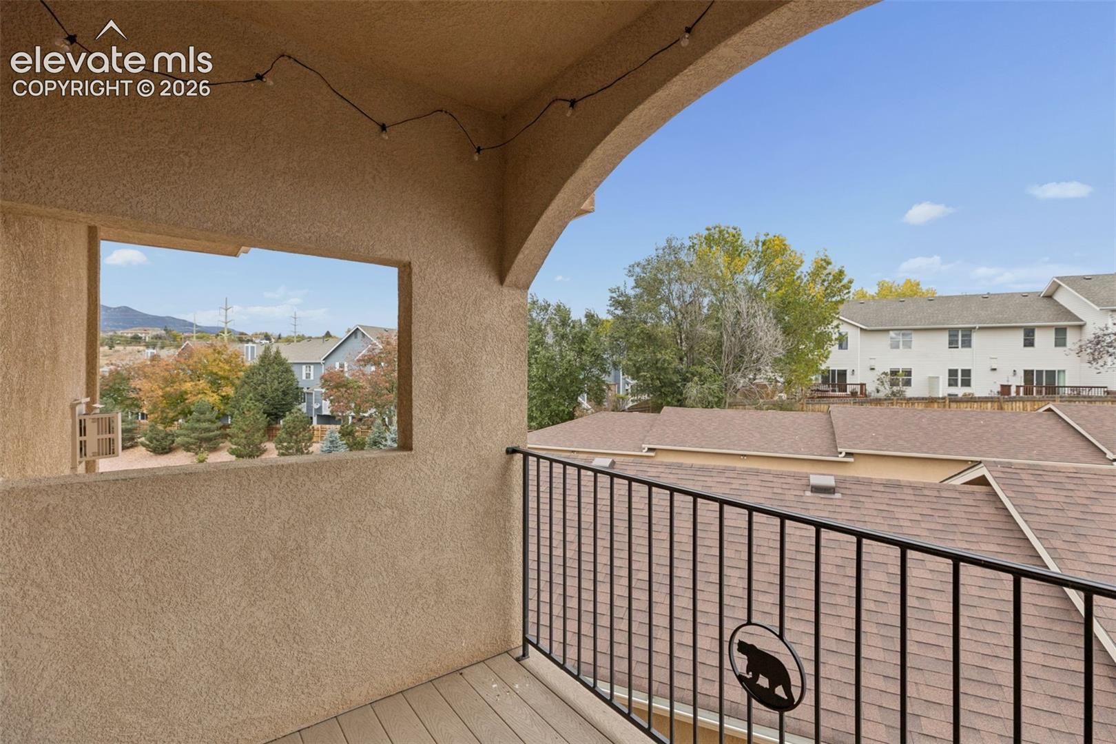 Covered balcony featuring textured stucco walls, composite decking, and black metal railing with decorative metal inlay