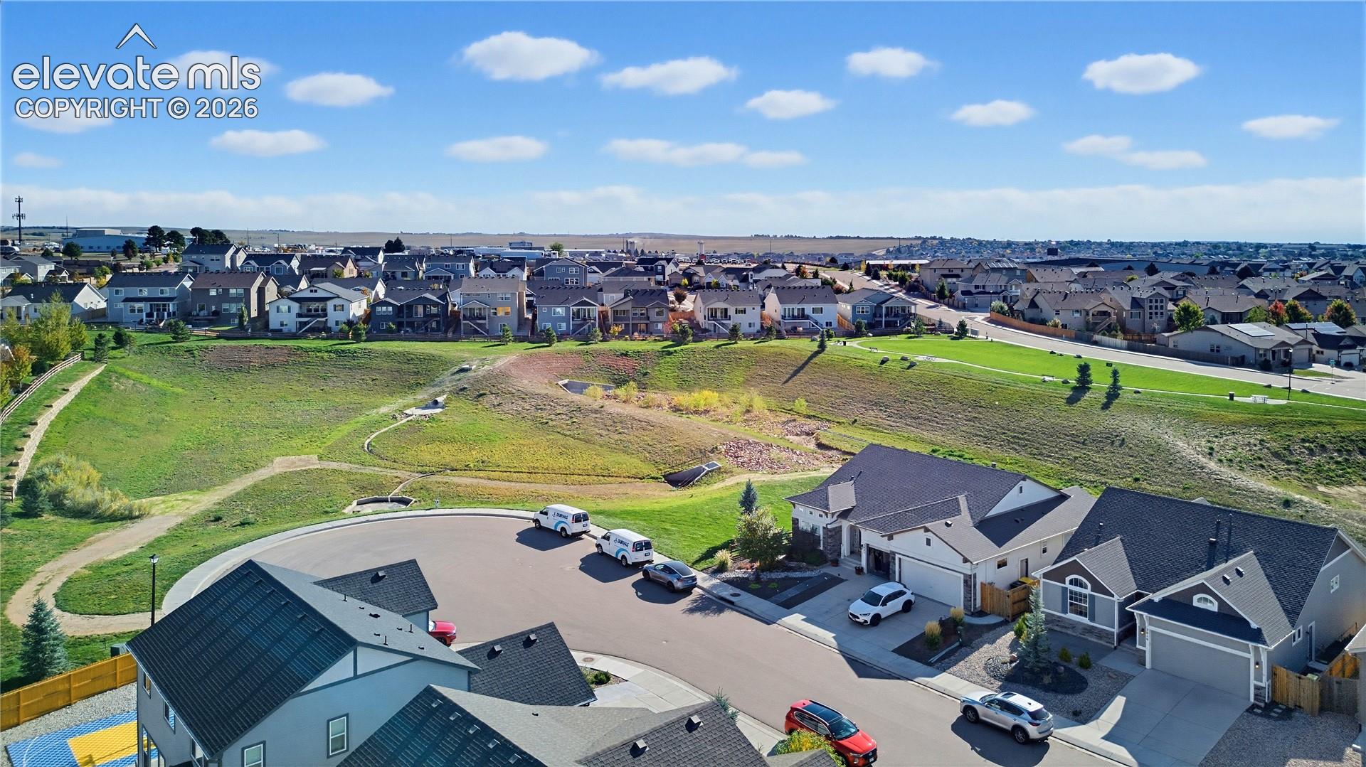 Aerial perspective showcasing a suburban residential layout featuring cul-de-sac positioning, multi-car garages, asphalt shingle roofing, and integrated community green space