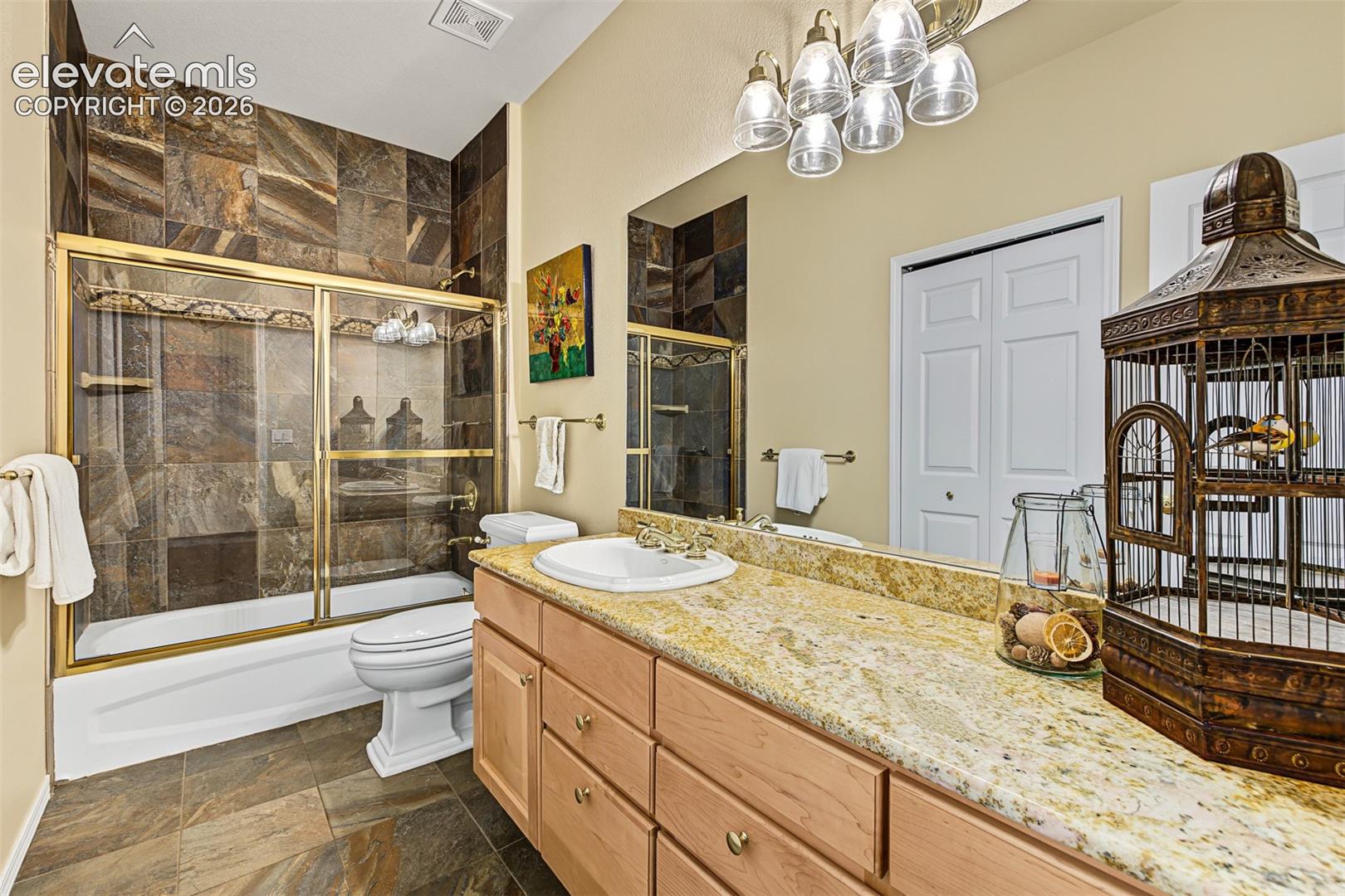 Full bathroom situated between two main-level bedrooms, featuring a granite vanity, tile flooring, and a tub/shower combination with floor-to-ceiling tile surround and glass enclosure.