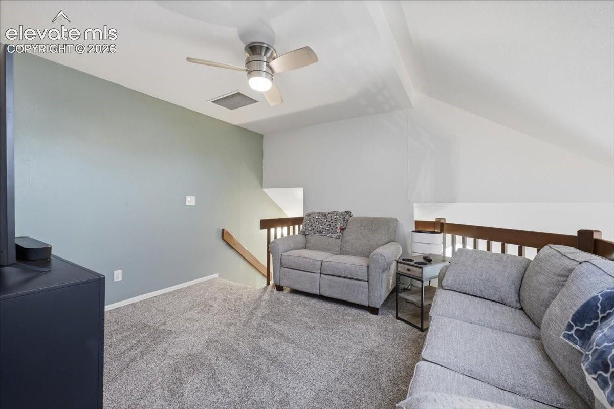 Vaulted ceilings, neutral carpeting, ceiling fan with integrated lighting, and wooden stair railing