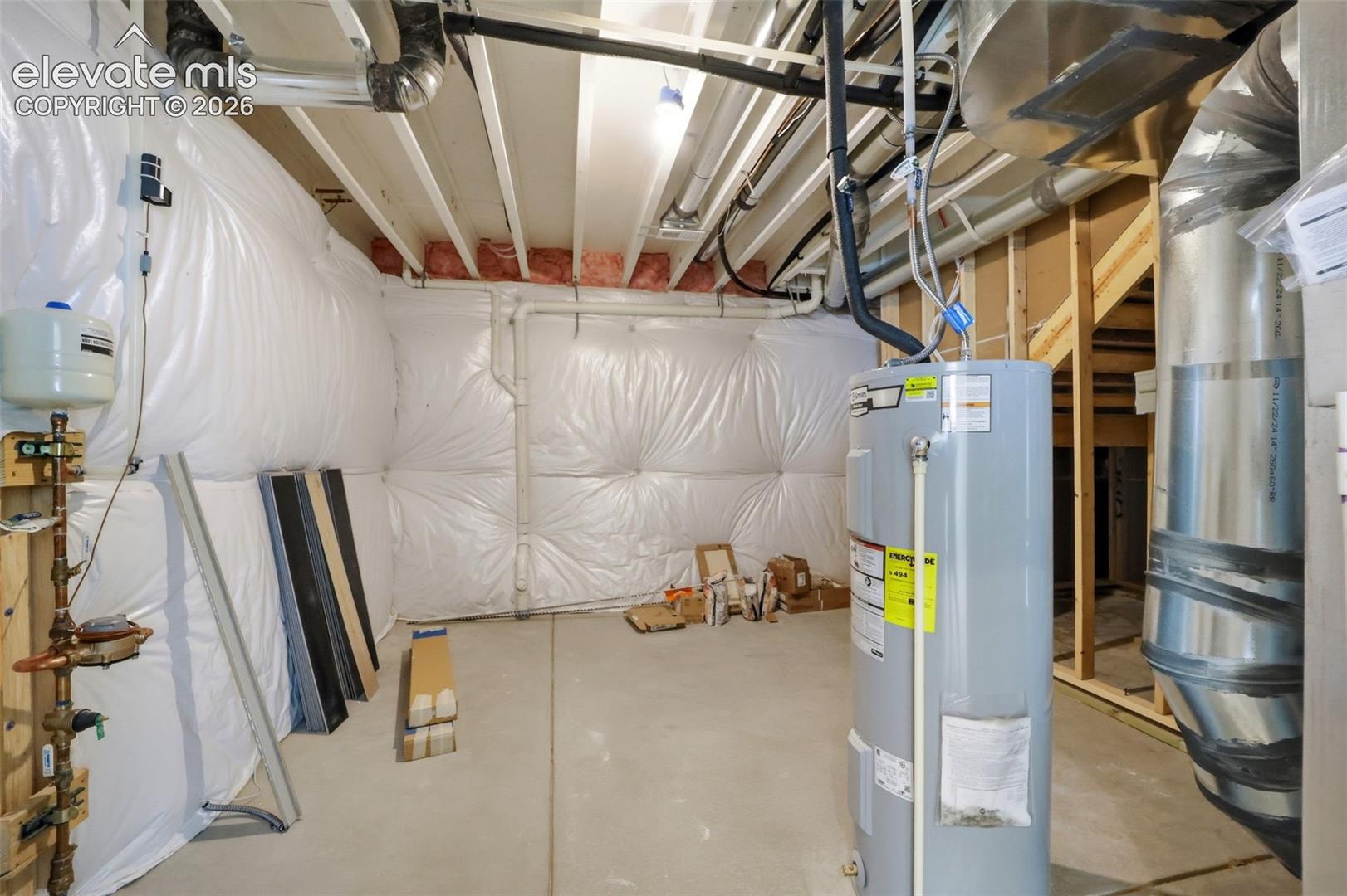 Unfinished utility area featuring a concrete floor, plastic vapor-barrier wall insulation, fiberglass batt ceiling insulation, a water heater, and exposed mechanical ductwork