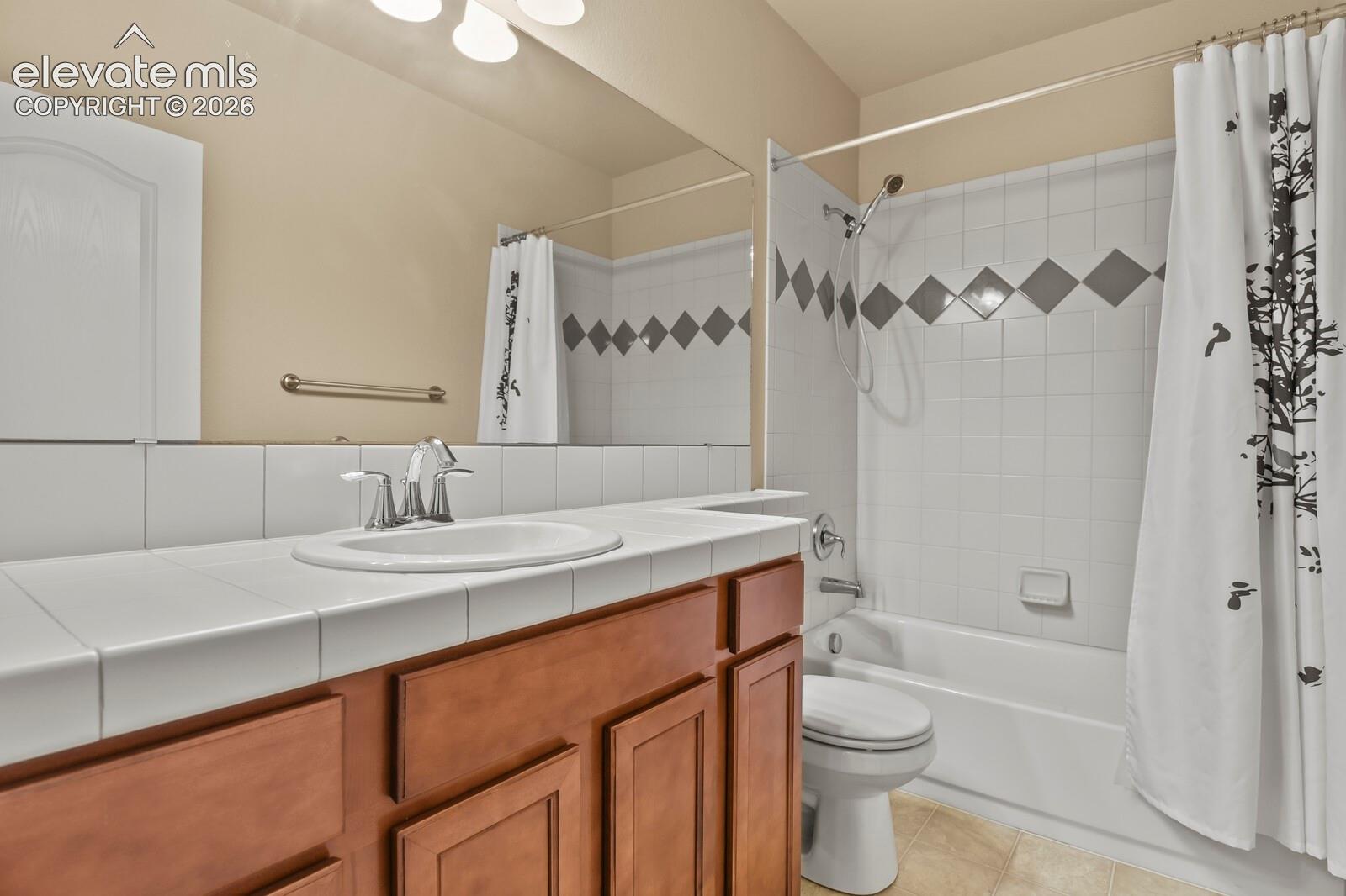 Vanity with a tiled countertop and integrated sink, chrome faucet, wood-finish cabinetry, and a full-width mirror