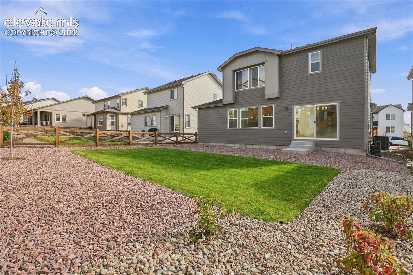 Rear exterior featuring horizontal siding, a sliding glass door, a fenced-in yard with a gravel border, and a rectangular lawn