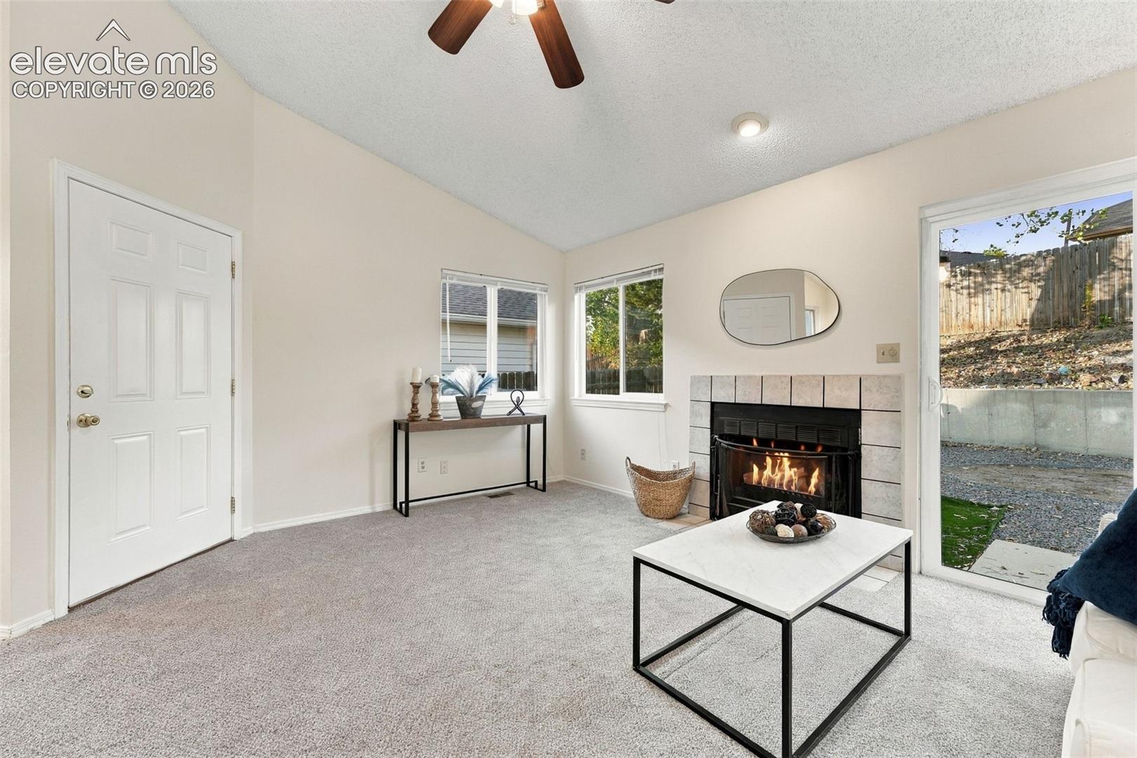 Vaulted ceiling featuring a ceiling fan, tiled fireplace surround, and sliding glass door with exterior access