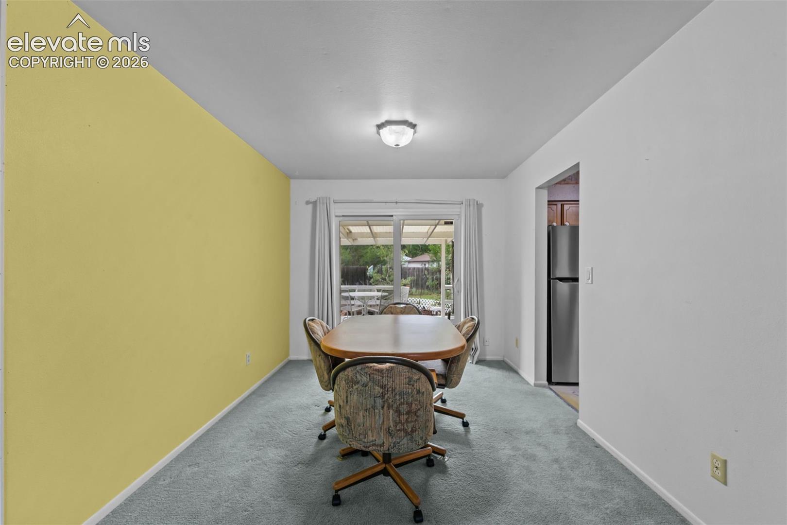 Recessed ceiling light fixture, sliding glass door with exterior access, light-toned carpeting, and a wall opening to an additional room