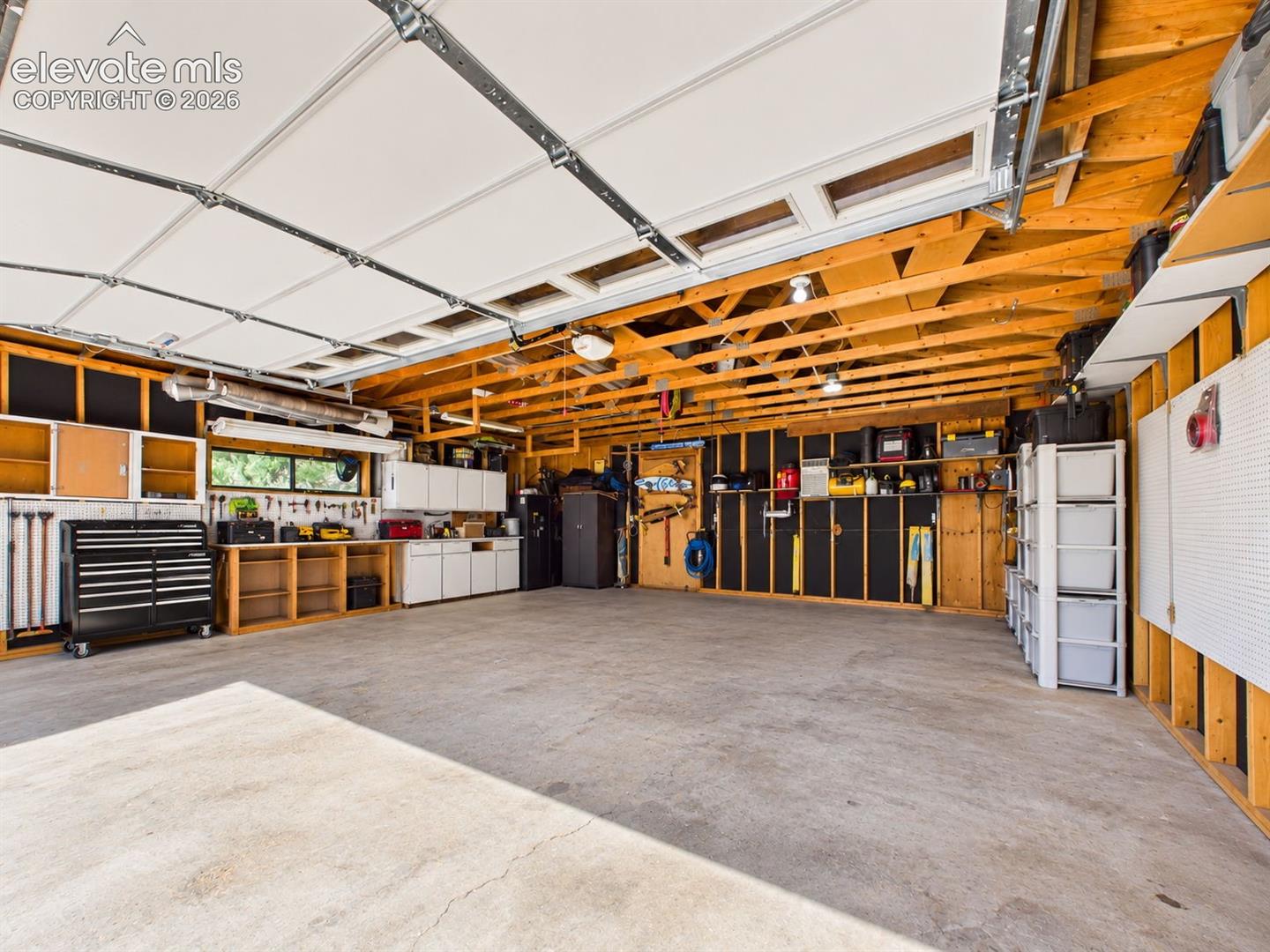Spacious garage features extensive wall storage, cabinetry, work surfaces, overhead lighting, and an open layout suited for parking or projects.