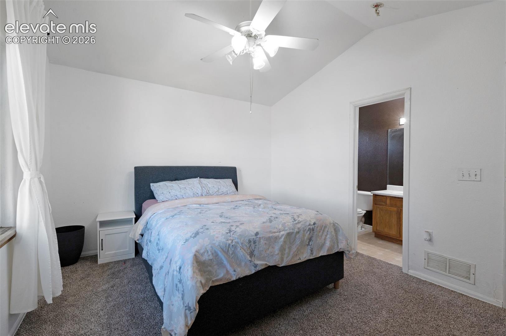 Bedroom featuring vaulted ceilings with a ceiling fan, carpet flooring, and an en-suite bathroom with a wood-finish vanity