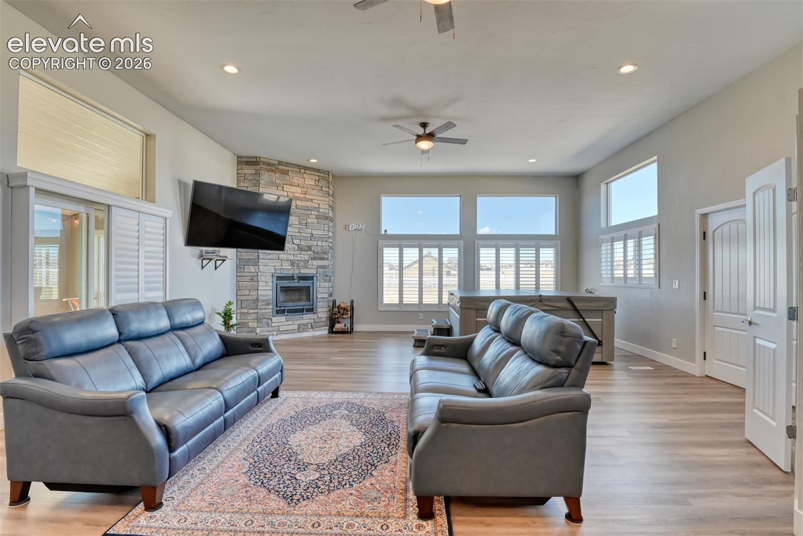 Spacious living area featuring high ceilings, recessed lighting, wood-finish flooring, wood burning fireplace, and multiple windows with plantation shutters.