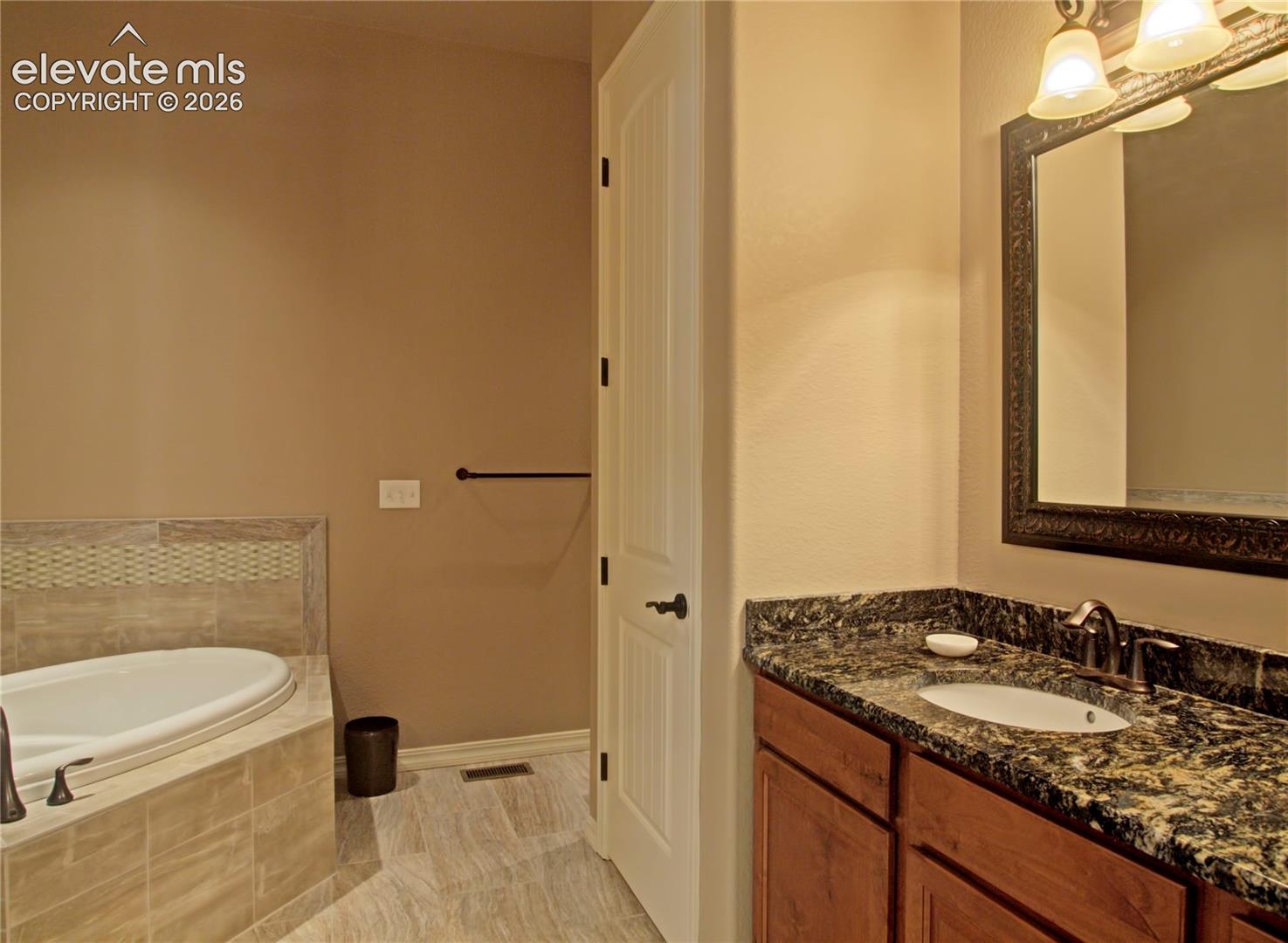 Bathroom featuring  5 piece bath and a built-in soaking tub with tile surround, a single vanity with stone countertop, and wood-finish cabinetry