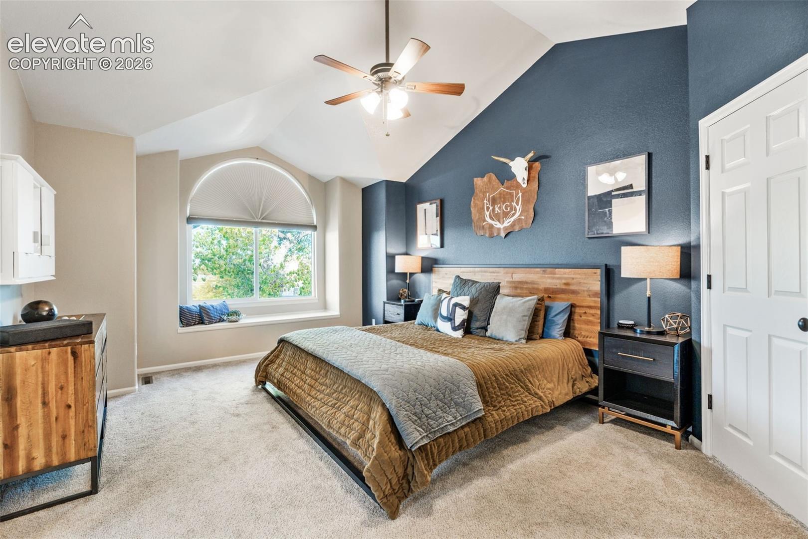 Vaulted ceiling with a centrally mounted ceiling fan, arched window with a built-in window seat, and neutral wall-to-wall carpeting