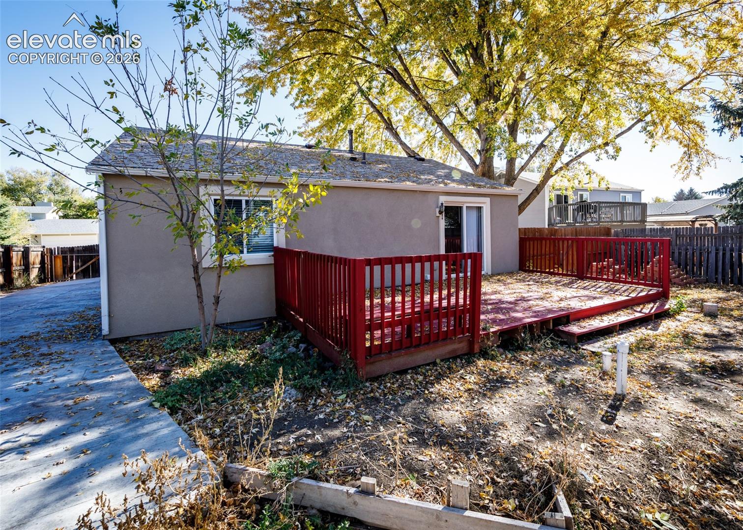 Rear exterior featuring a raised wood deck with railing, sliding glass door, and paved driveway