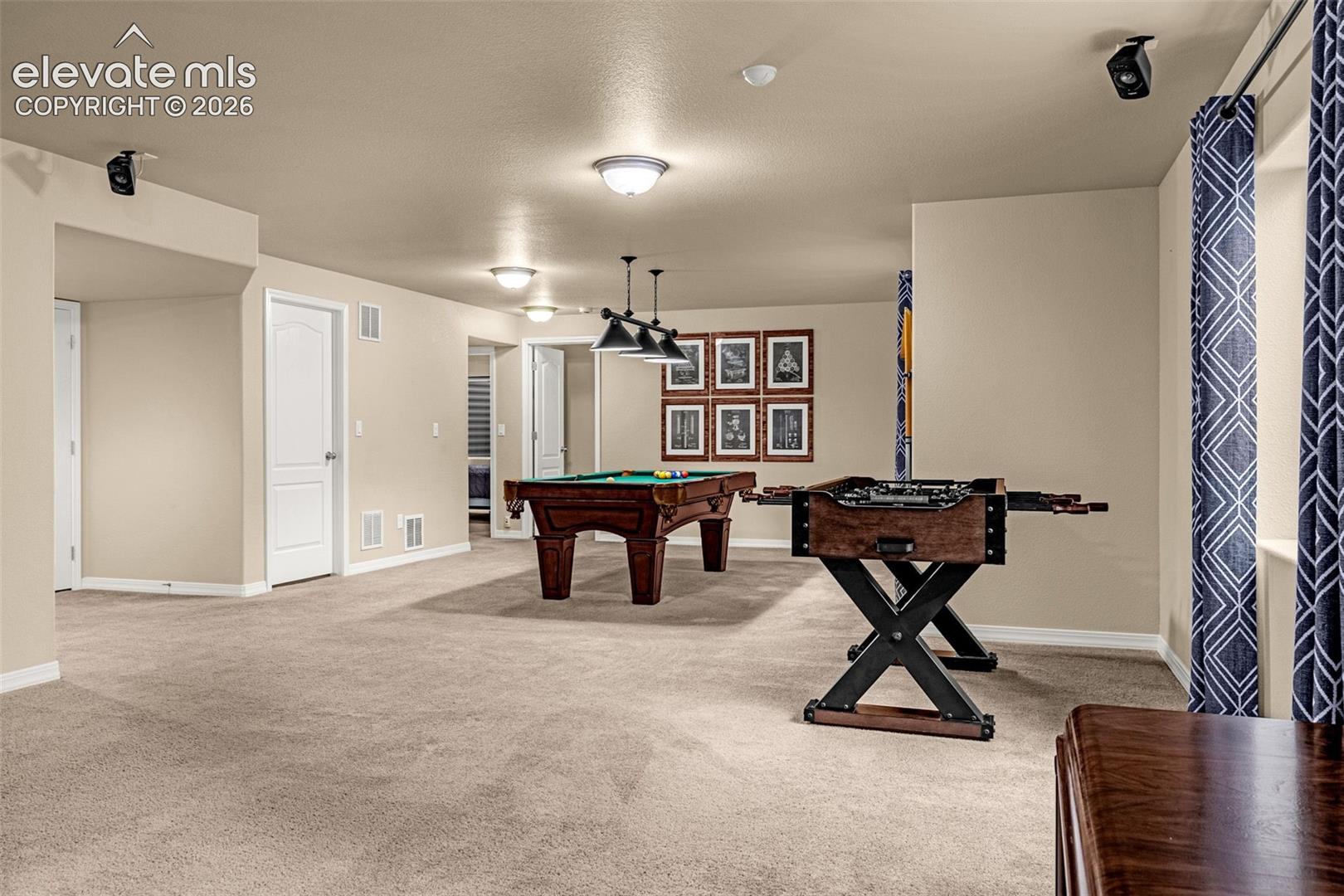 Interior space featuring neutral wall tones, wall-mounted audio speakers, recessed ceiling lighting, and a three-light metal billiard fixture