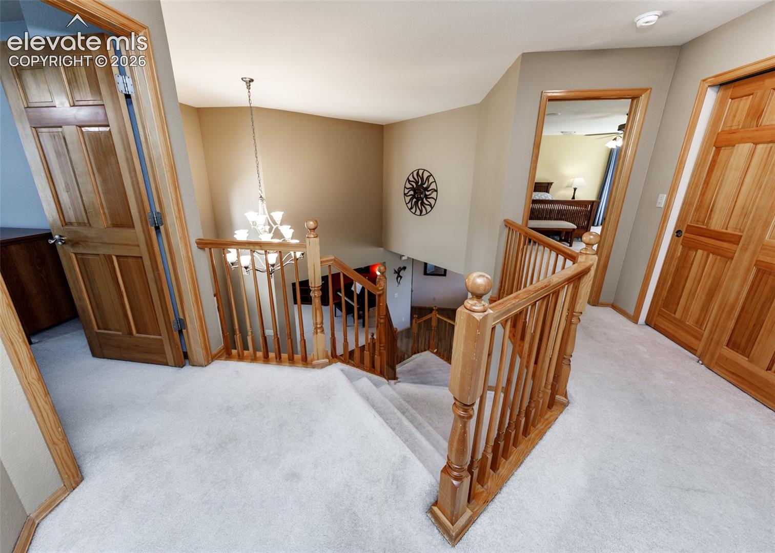 Staircase featuring natural wood handrails and balusters, multi-light hanging chandelier, and wood-paneled interior doors