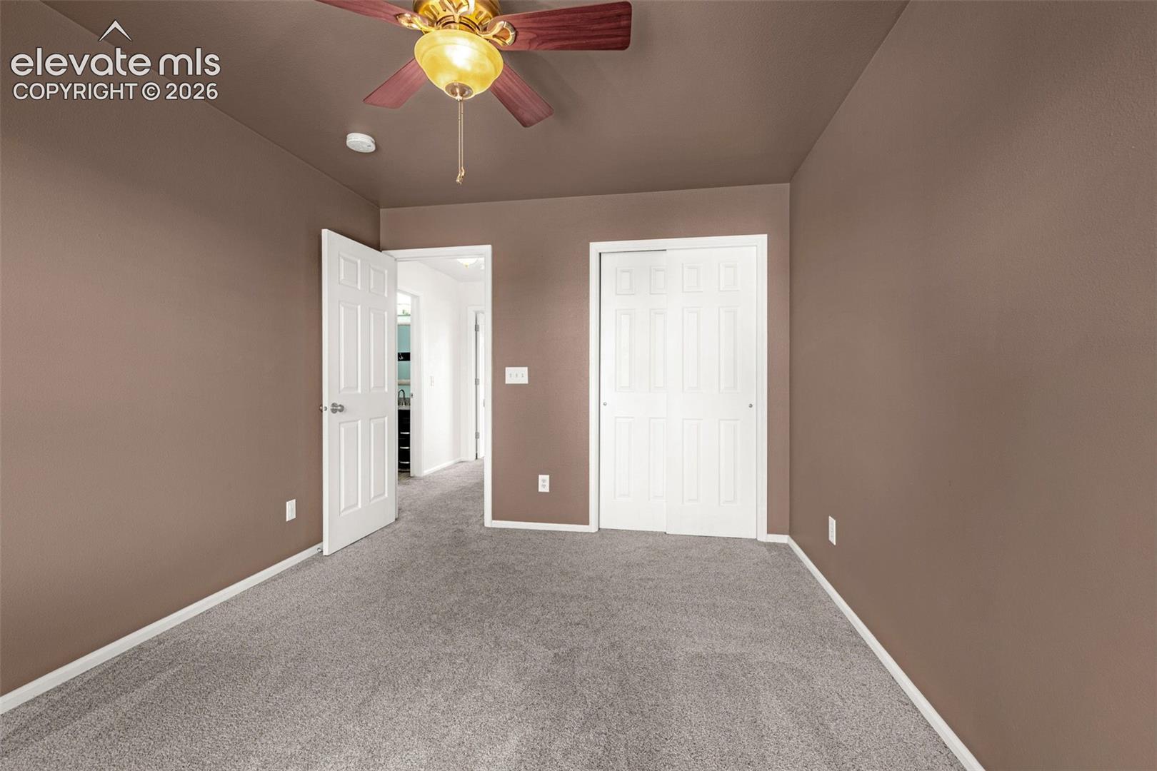 Room featuring neutral wall tones, carpeted flooring, a ceiling fan with integrated lighting, a sliding-panel closet, and a multi-panel interior door