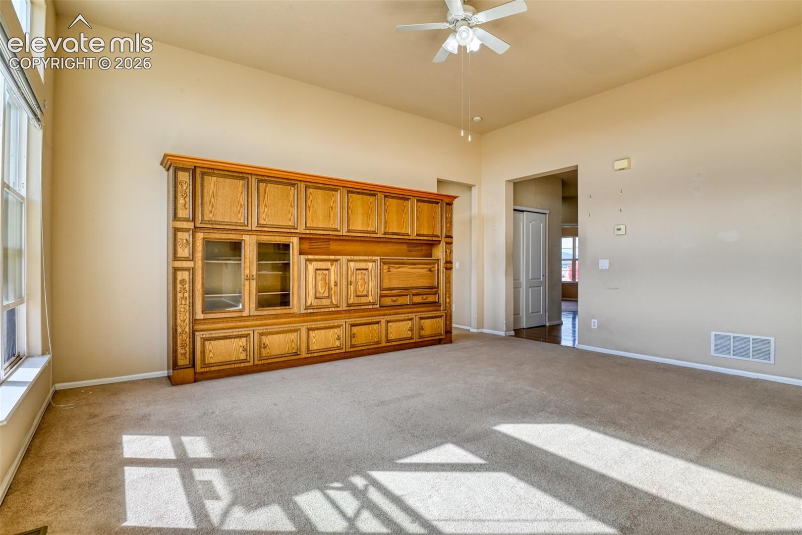 High ceilings, custom built-in wood cabinetry, expansive windows, carpeted flooring, and a ceiling fan