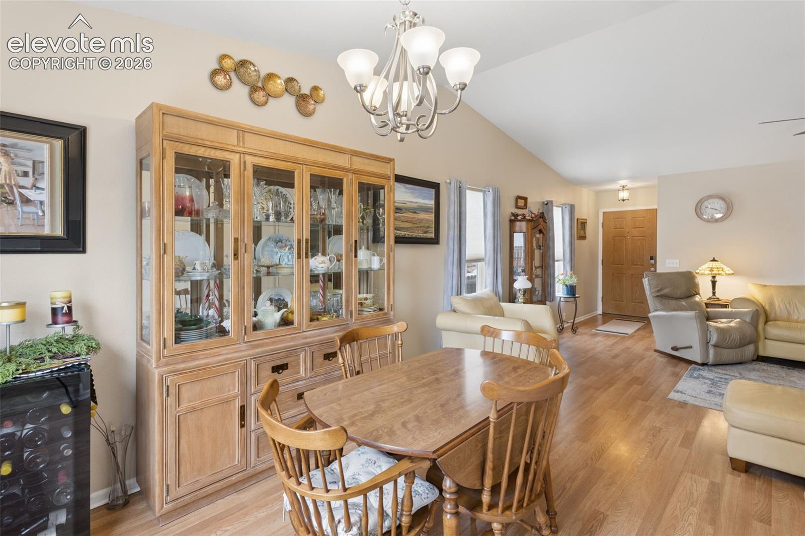 Vaulted ceiling, wood-finish flooring, light tan wall color, built-in display cabinetry, and a prominent chandelier