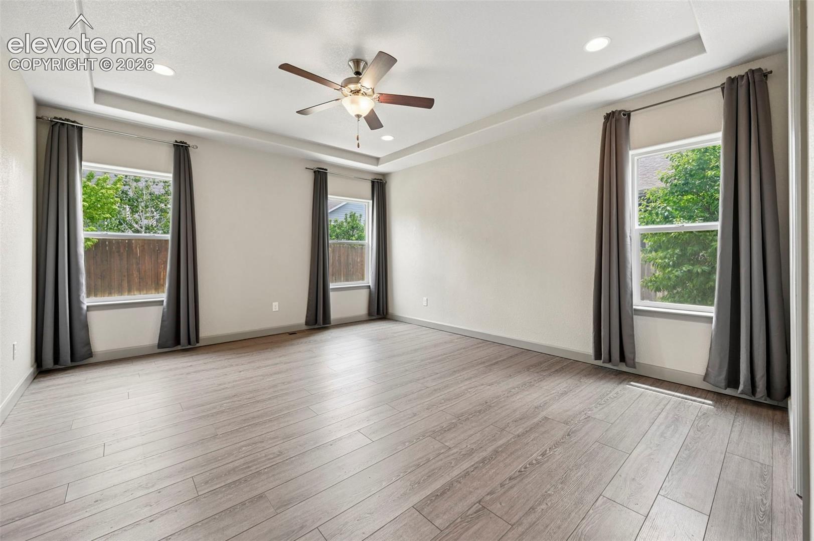 Tray ceiling with recessed lighting, wood-finish flooring, and a central ceiling fan with integrated light fixture