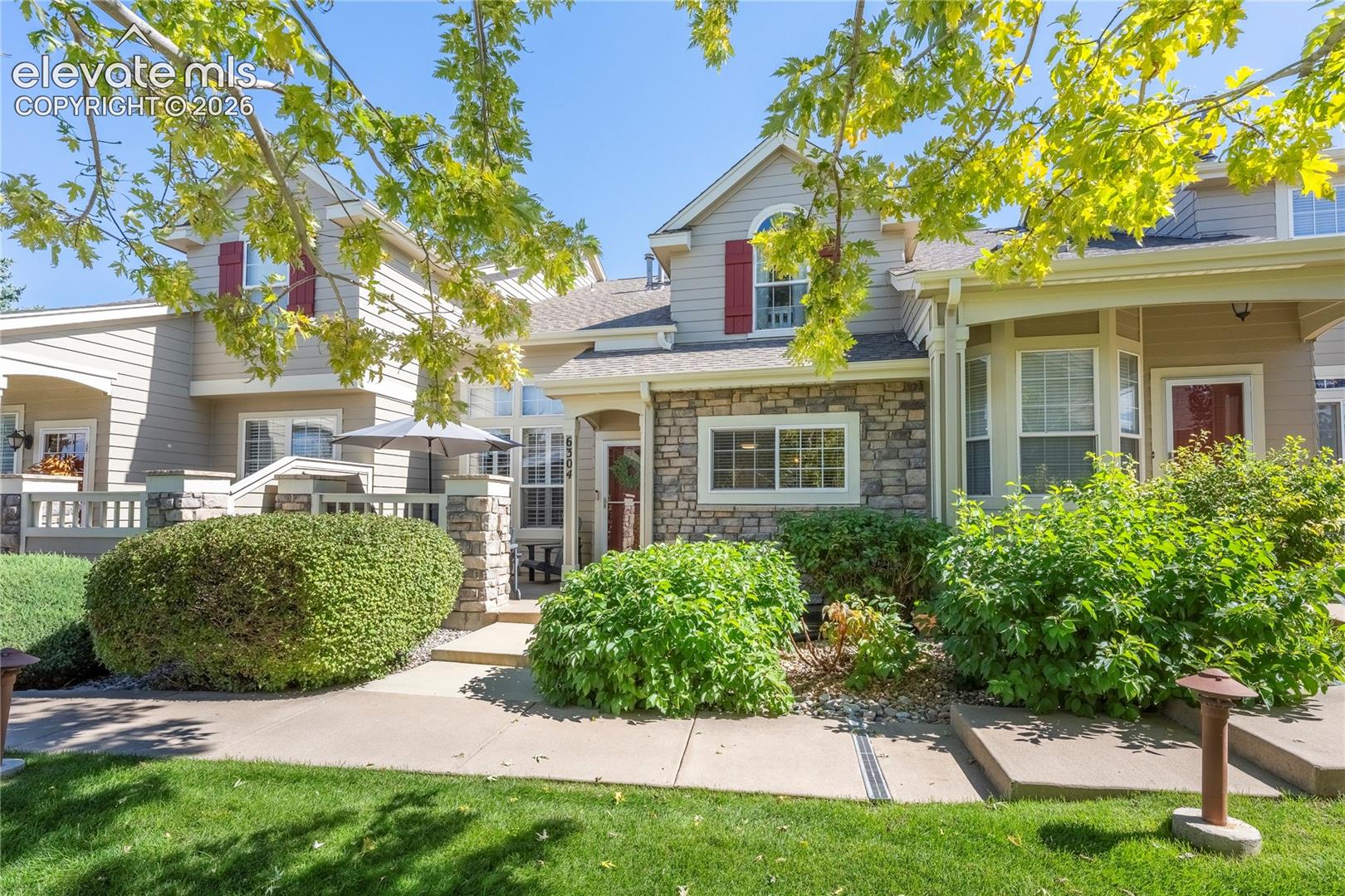 Exterior featuring multi-textured facade with horizontal siding and stone veneer, decorative red shutters, covered front porch, and manicured landscaping